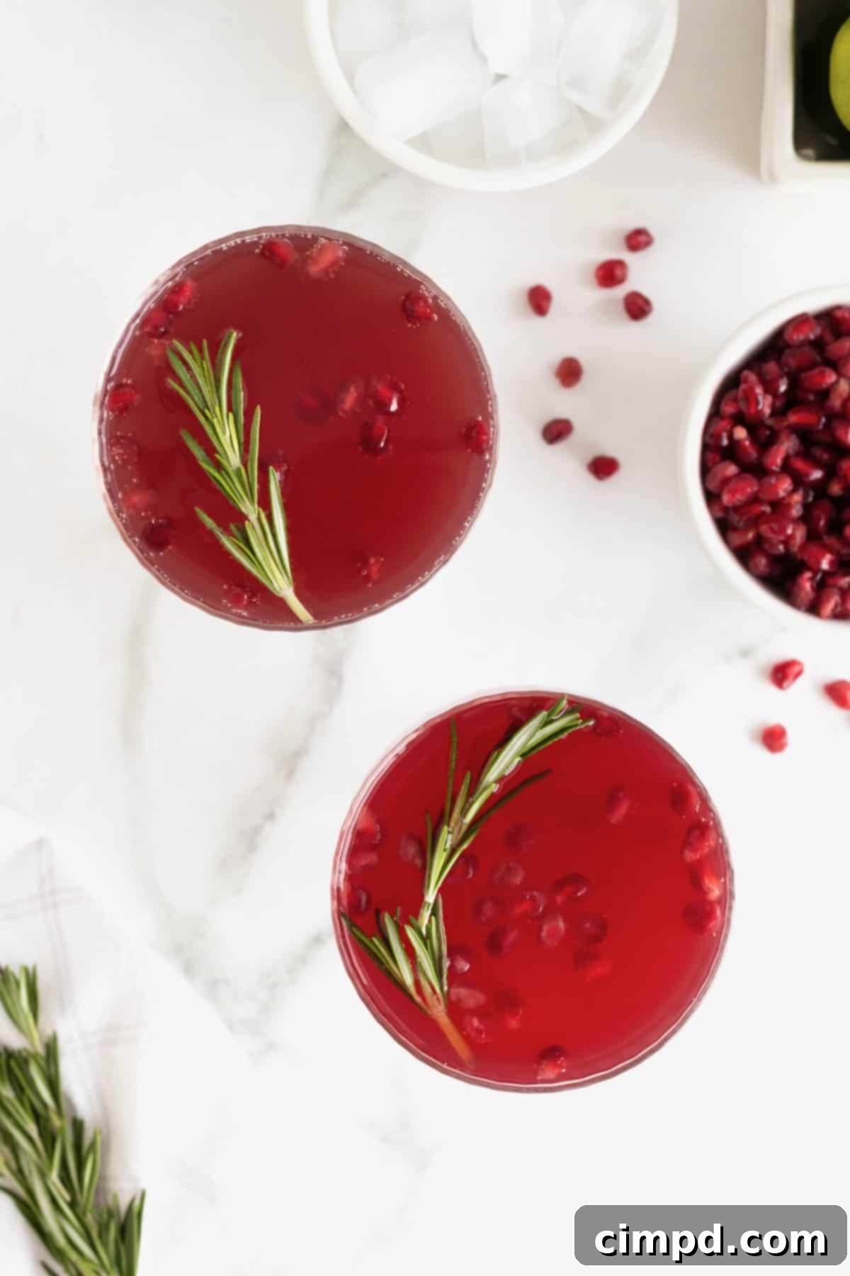 Two beautiful Pomegranate Rosemary Holiday Cocktails showcased in elegant coupe glasses, garnished with fresh pomegranate seeds and fragrant rosemary sprigs, perfect for holiday celebrations.