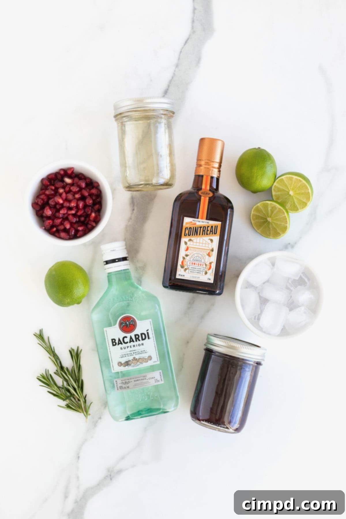A curated display of ingredients laid out on a white marble counter, ready to be transformed into a refreshing Pomegranate Rosemary Holiday Cocktail.