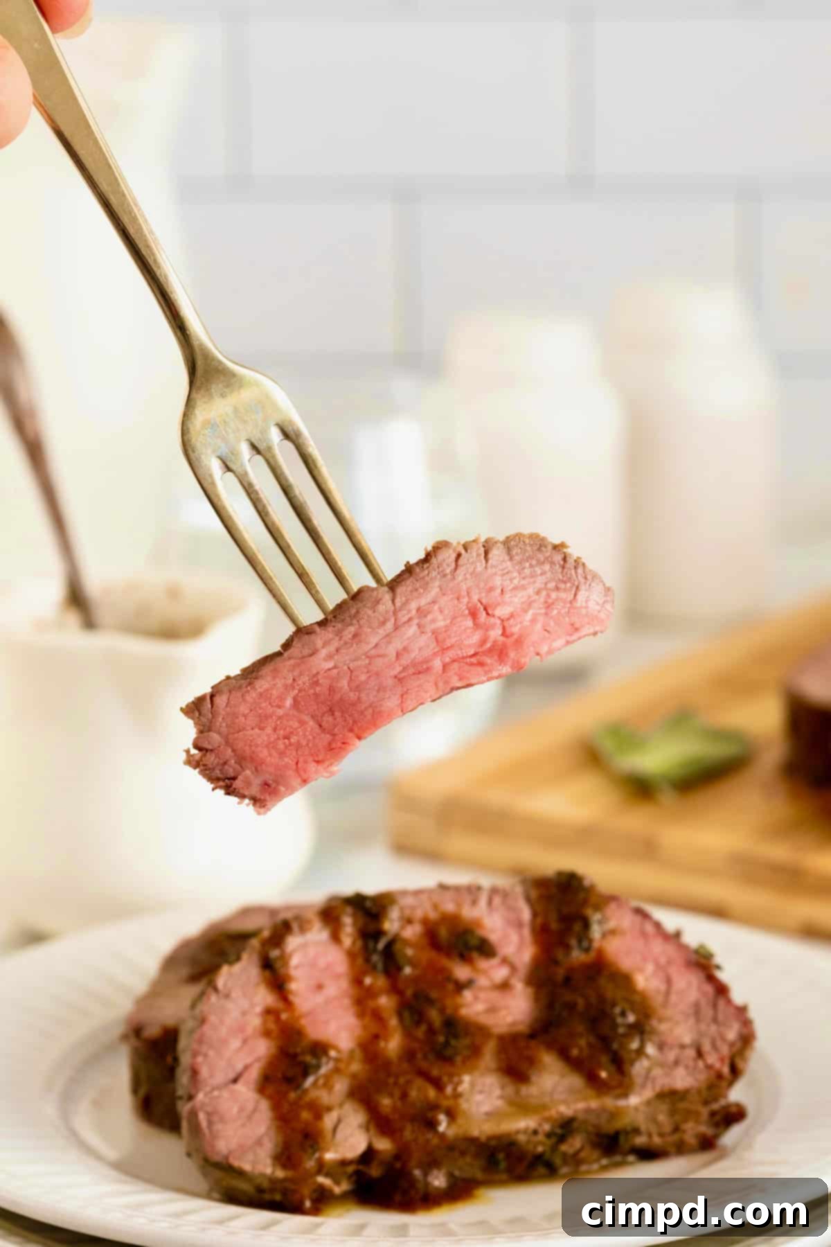 Herb-Crusted Beef Tenderloin 3 A piece of beef tenderloin on a fork above a plate of sliced beef tenderloin in pan sauce.