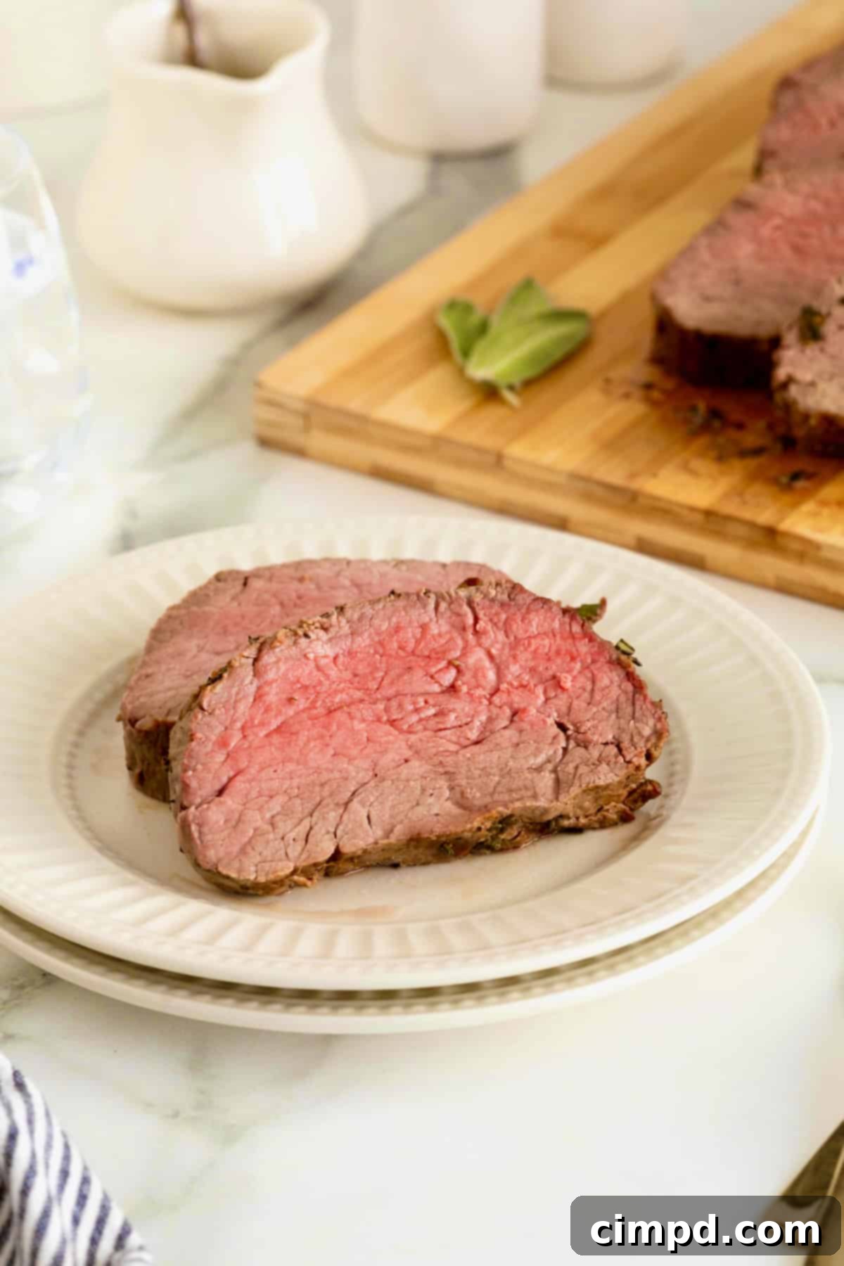 Herb-Crusted Beef Tenderloin 4 Two slices of beef tenderloin on a small white fluted plate.