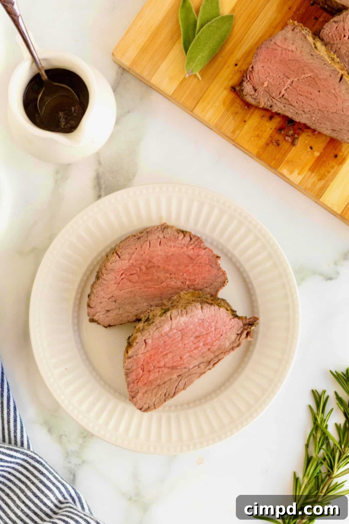 Herb-Crusted Beef Tenderloin 5 Two slices of beef tenderloin on a small white fluted plate.
