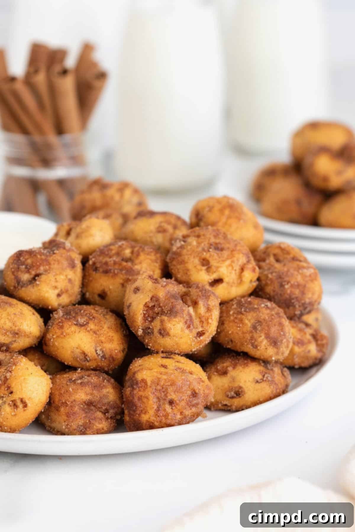A large white serving plate featuring a generous helping of golden cinnamon roll bites, with a small white bowl of creamy icing placed alongside, ready for enjoyment.