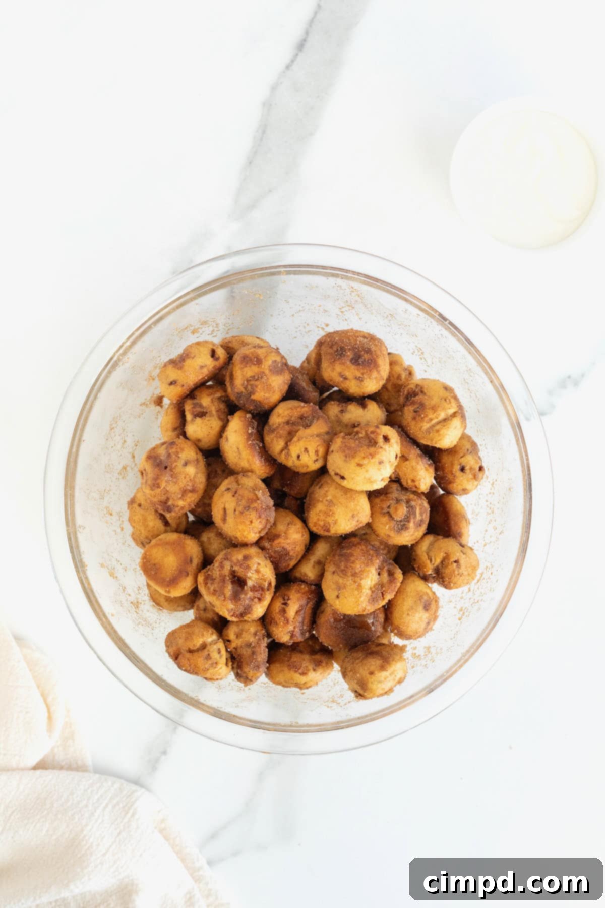 A clear glass bowl generously filled with freshly made cinnamon roll bites, glistening with their perfect cinnamon sugar coating.