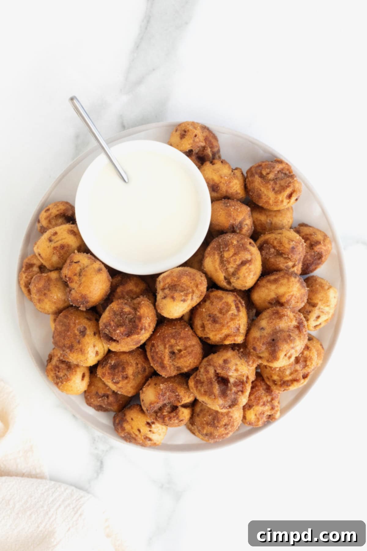 A pristine white serving plate artfully arranged with a bounty of warm, cinnamon-sugar-coated cinnamon roll bites, accompanied by a small, inviting bowl of white icing for dipping.