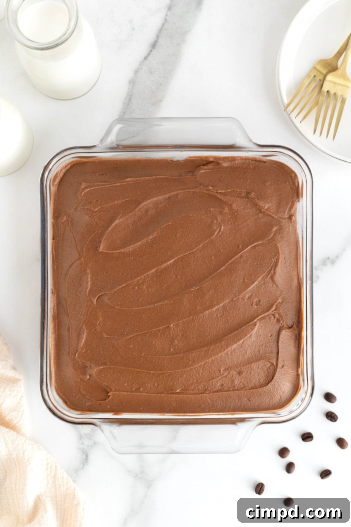 Mocha Velvet Brownies 11 A square glass baking dish of frosted brownies on a white marble counter.