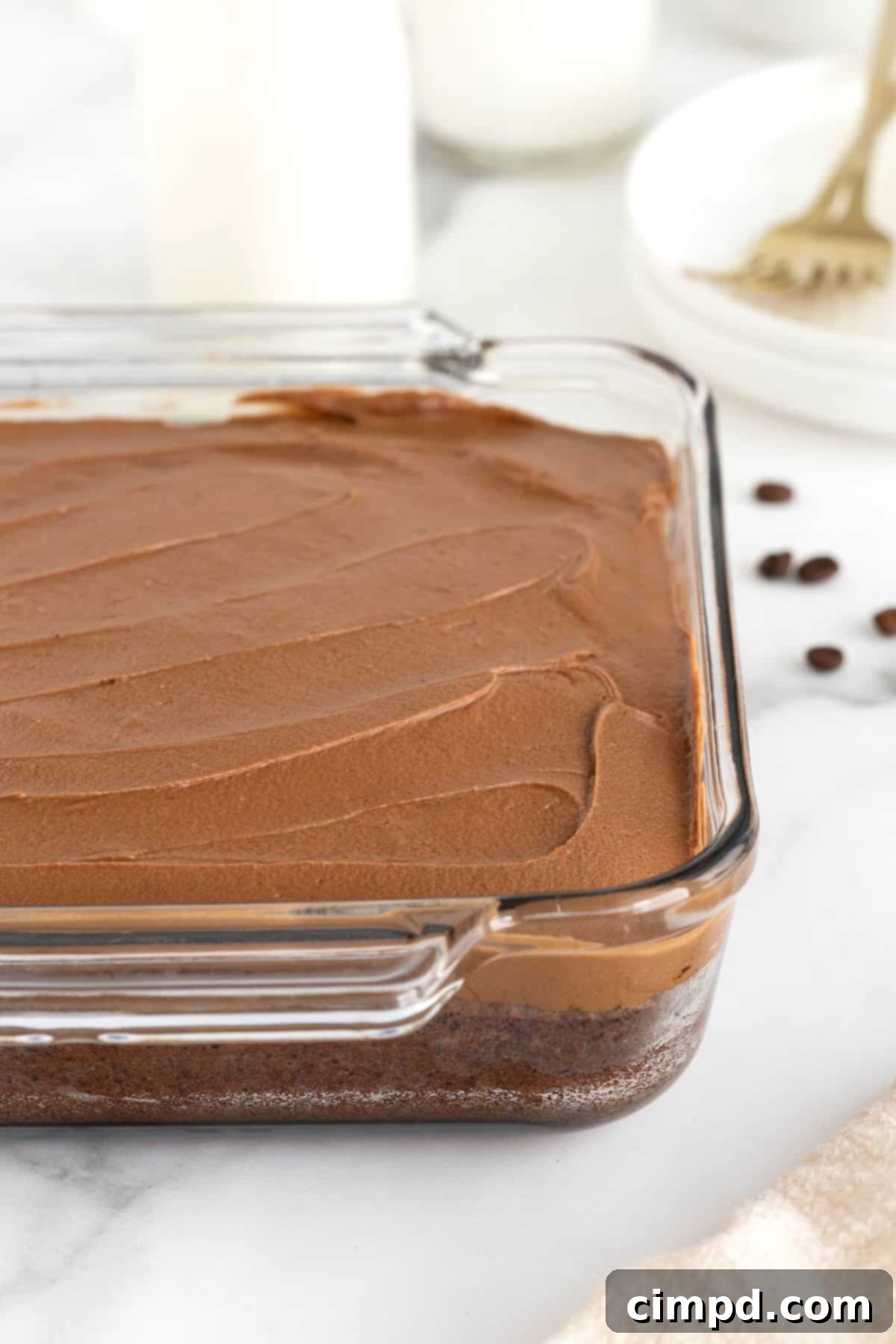 Mocha Velvet Brownies 12 A square glass baking dish of frosted brownies on a white marble counter.