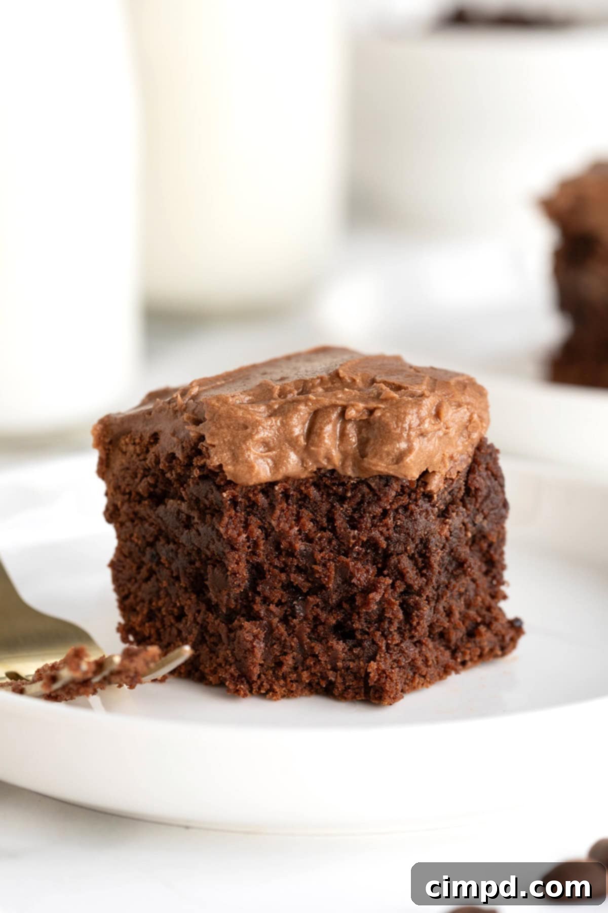 Mocha Velvet Brownies 3 A frosted brownie on a small white rimmed plate next to a fork.