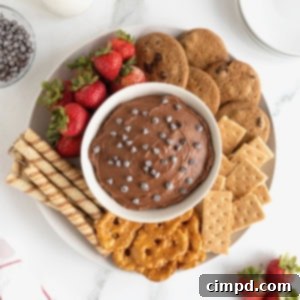 Decadent Chocolate Cheesecake Dip 9 A white bowl of chocolate cheesecake dip topped with chocolate chips and surrounded with various crackers, cookies, pretzels and strawberries.