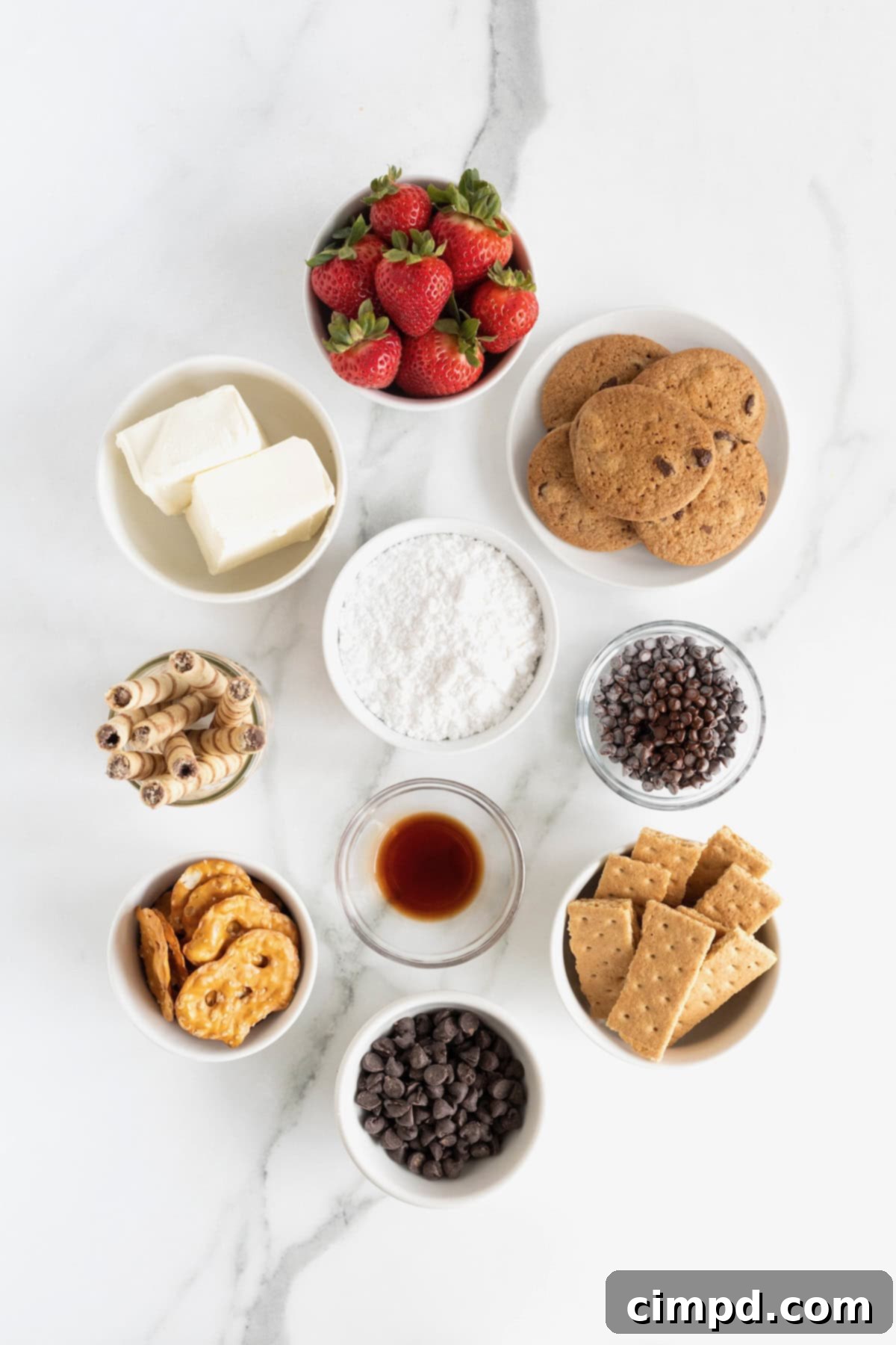 Decadent Chocolate Cheesecake Dip 5 Ingredients for chocolate cheesecake dip including cream cheese, powdered sugar, vanilla, and chocolate chips in small white and glass bowls, arranged on a white marble countertop.