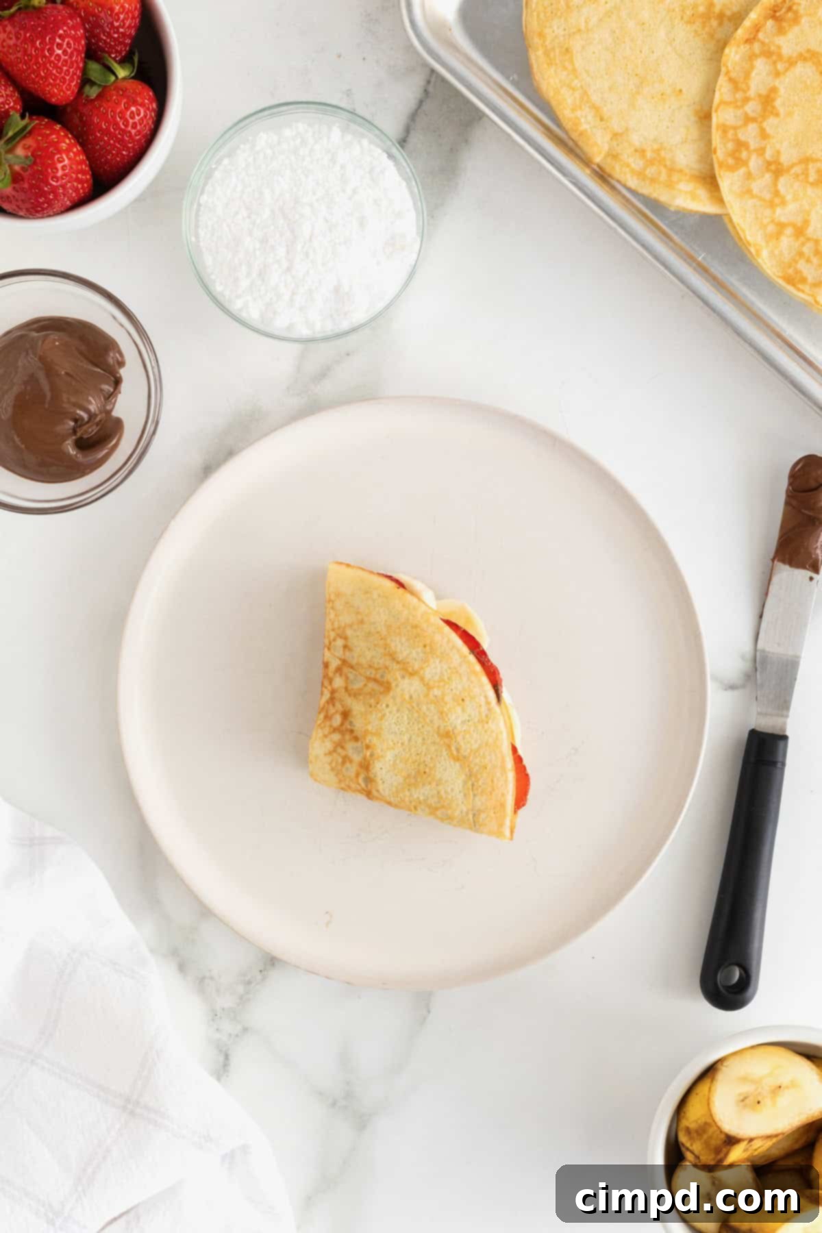 A perfectly folded sweet crepe, showcasing its elegant quarter-fold, resting on a white fluted plate, ready for its final garnish.