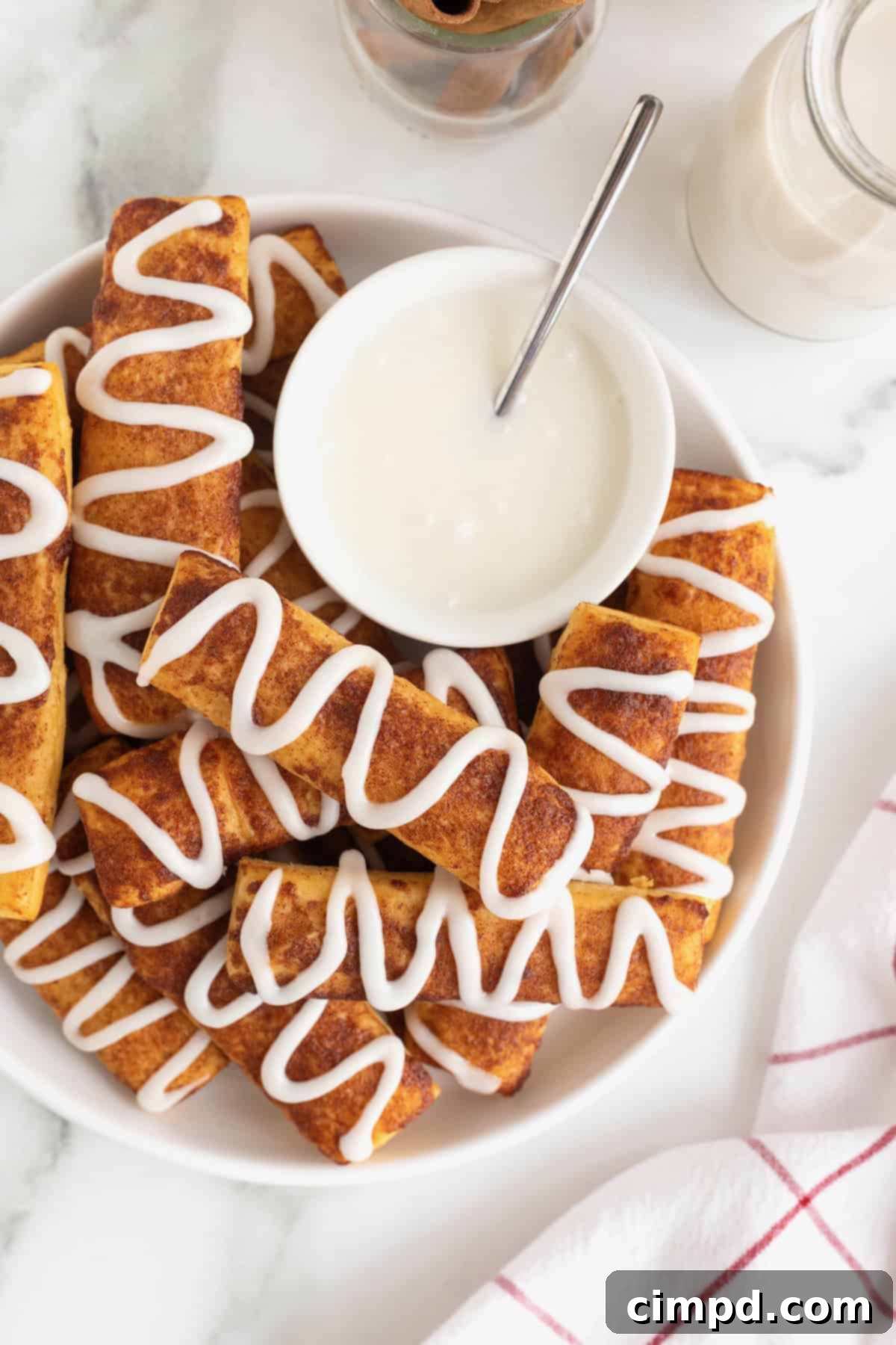 Gooey Cinnamon Fries 2 A large white serving plate of cinnamon roll sticks surrounding a bowl of white icing.