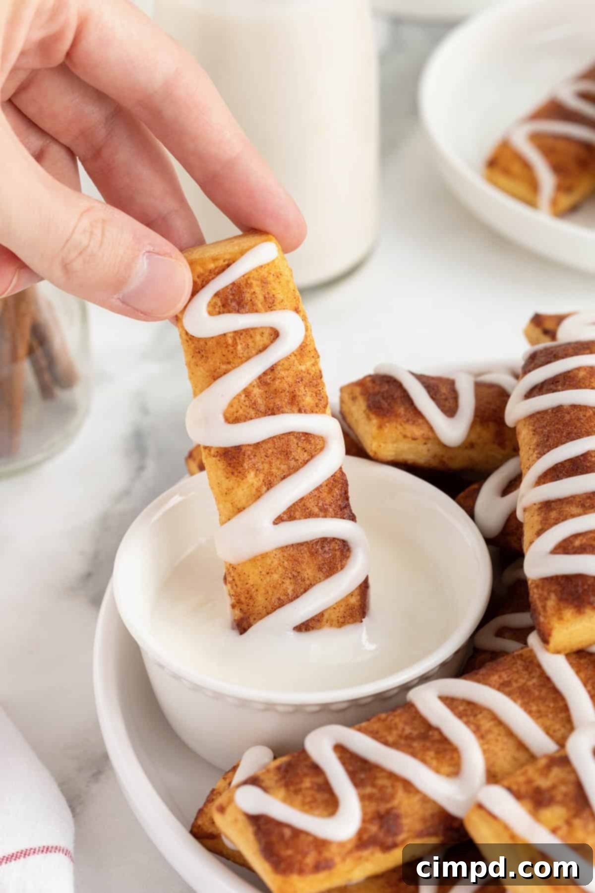 Gooey Cinnamon Fries 3 A hand dipping cinnamon roll stick into white icing.