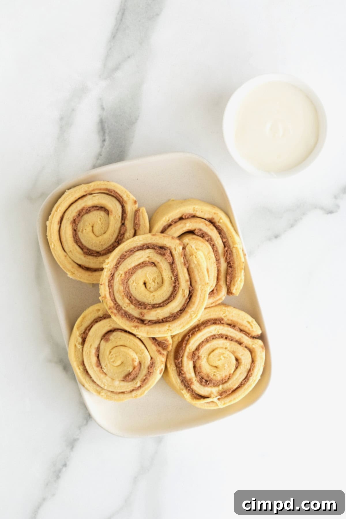 Gooey Cinnamon Fries 5 A white rectangular plate of canned cinnamon rolls next to a small white dish of icing on a white marble counter.