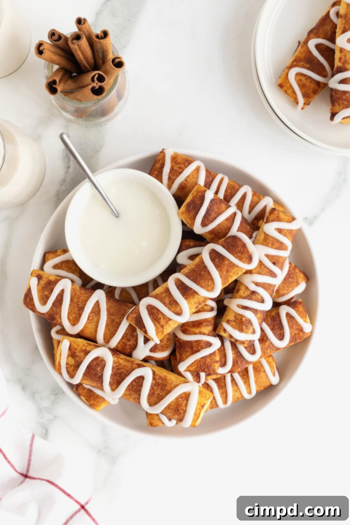 Gooey Cinnamon Fries 7 A large white serving plate of cinnamon roll sticks surrounding a bowl of white icing.