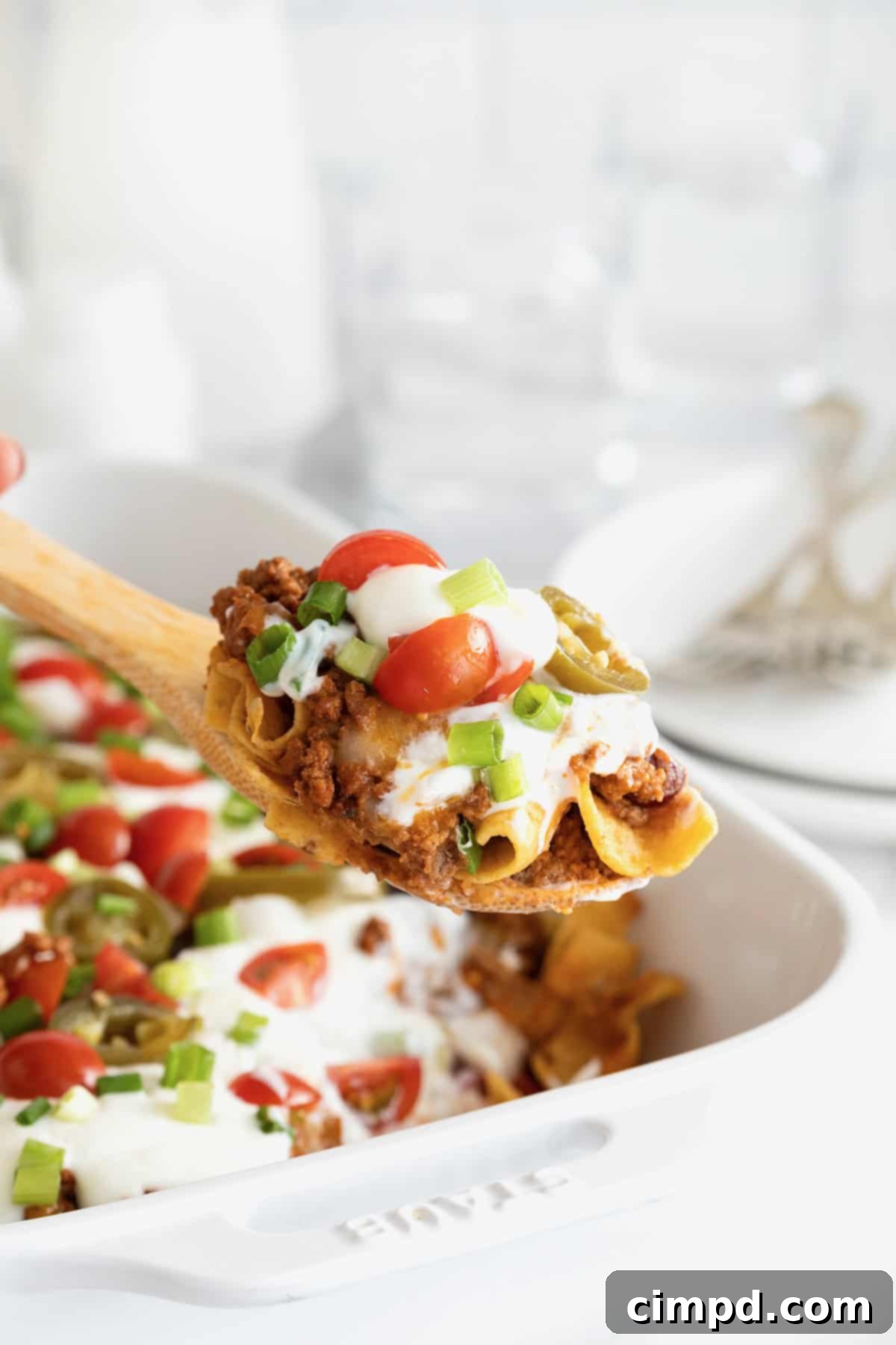 Loaded Frito Chili Bake 4 A serving of Frito chili pie casserole scooped onto a wooden spoon, held above the casserole dish.