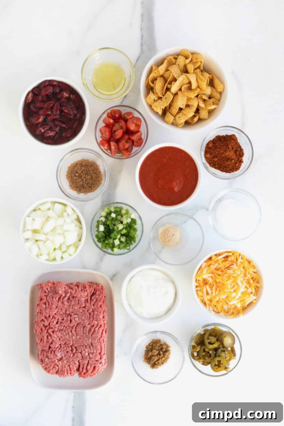 Loaded Frito Chili Bake 5 Various ingredients for Frito Chili Pie Casserole, portioned into small glass dishes on a white marble counter.
