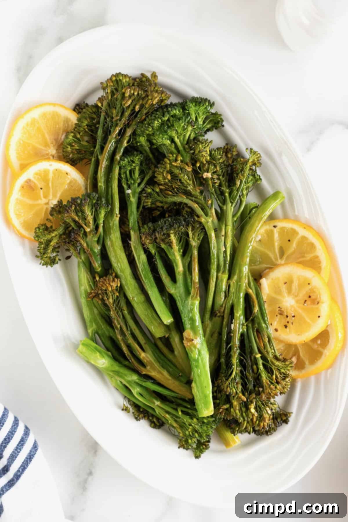 A white oval serving platter of broccolini and lemon slices, beautifully garnished and ready to serve.