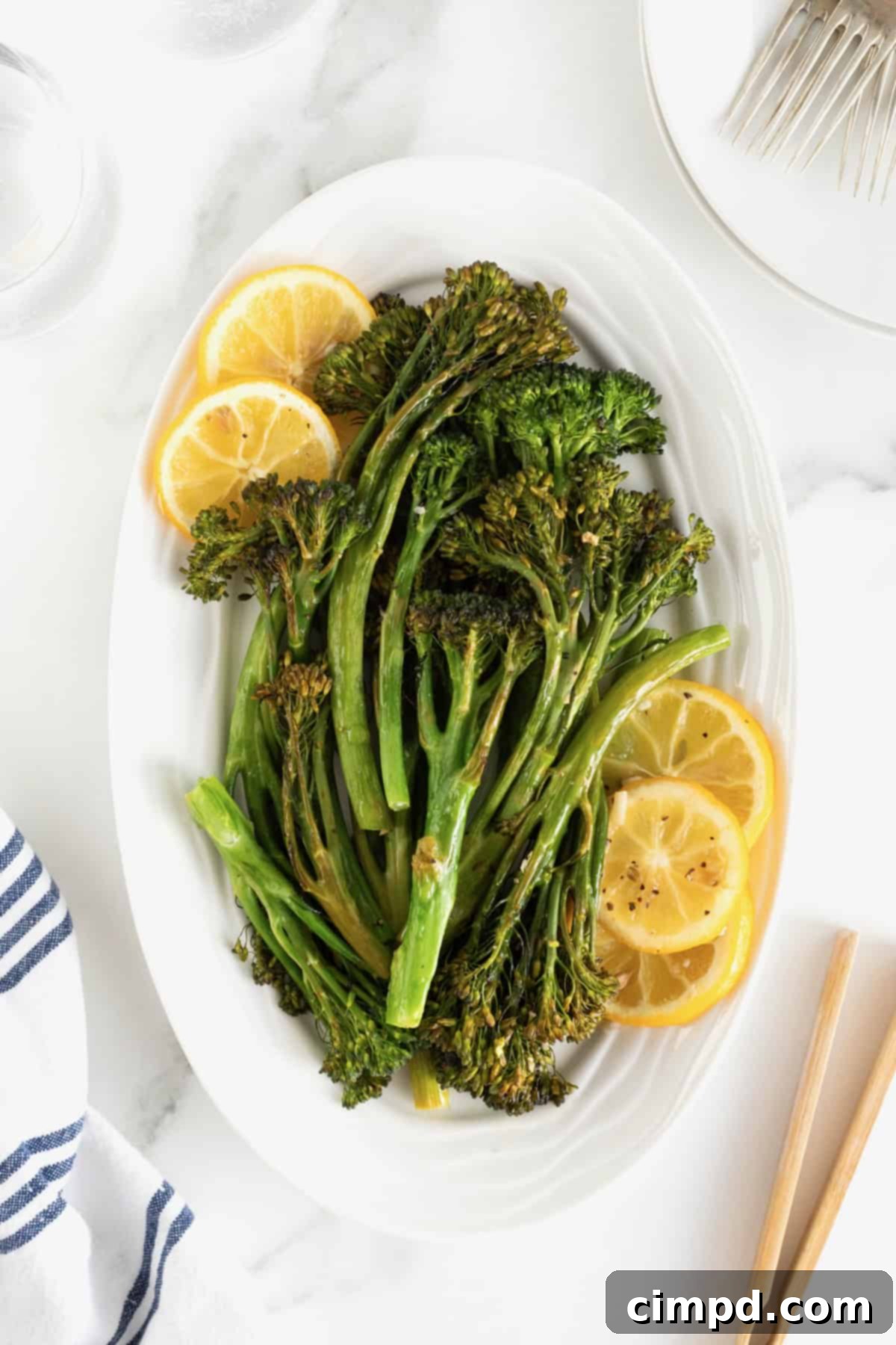 A generous pile of roasted broccolini, garnished with bright lemon slices, arranged artfully on an oval white serving platter.