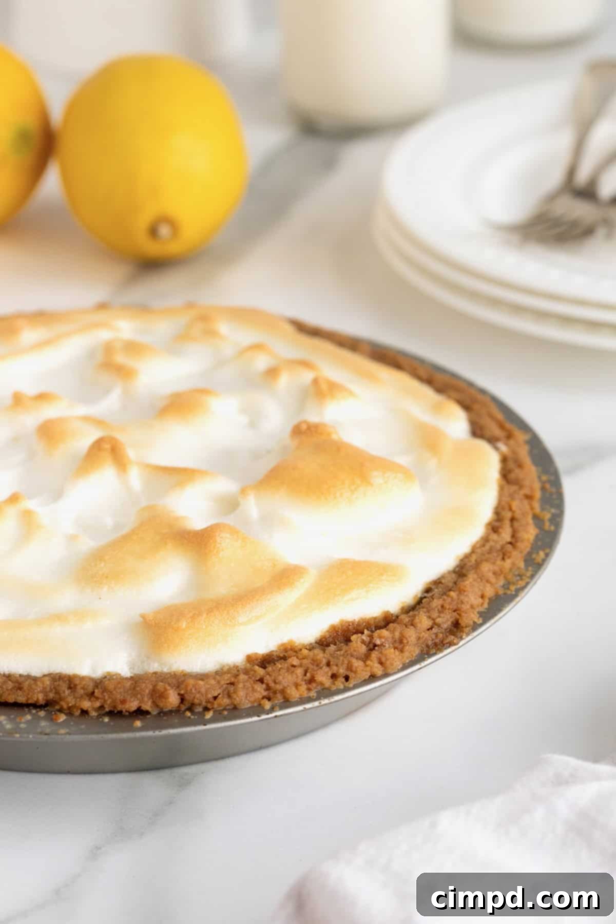 Zesty Meringue Dream 3 A pristine Lemon Meringue Pie in a rustic aluminum pie plate, glistening on a elegant white marble kitchen counter, ready to be sliced.