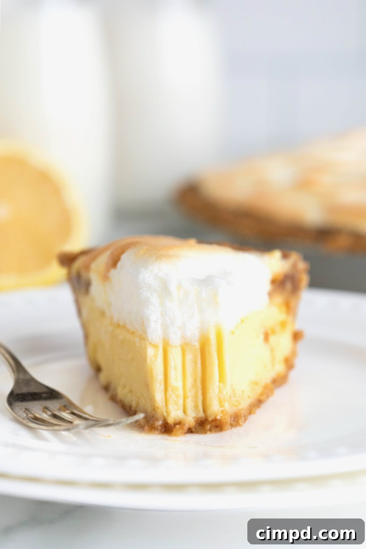 Zesty Meringue Dream 4 A tantalizing slice of Lemon Meringue Pie presented on a white plate, with a fork poised nearby. A small bite has been taken, revealing the layers of fluffy meringue and creamy lemon filling.
