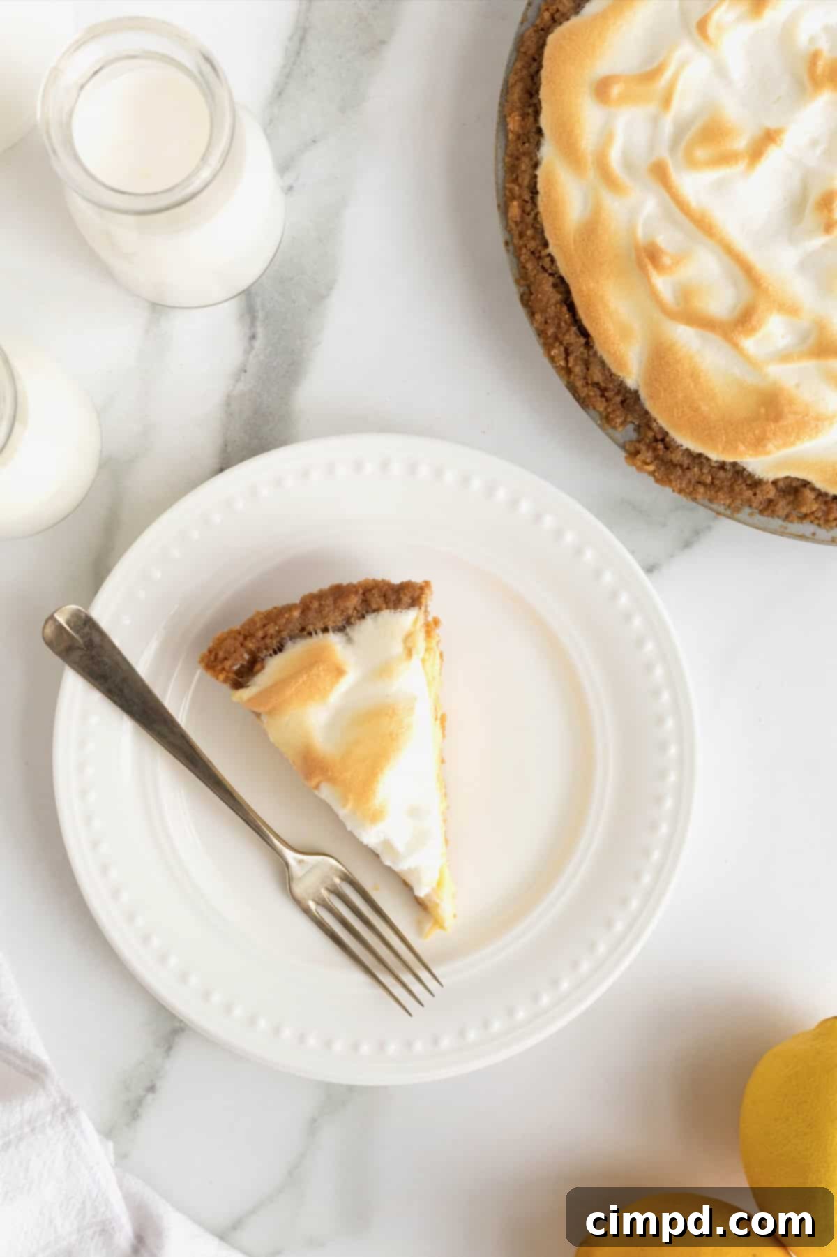 Zesty Meringue Dream 5 A pristine slice of Lemon Meringue Pie, perfectly portioned and ready to be enjoyed, displayed next to a fork on a elegant white dessert plate with delicate beaded accents.