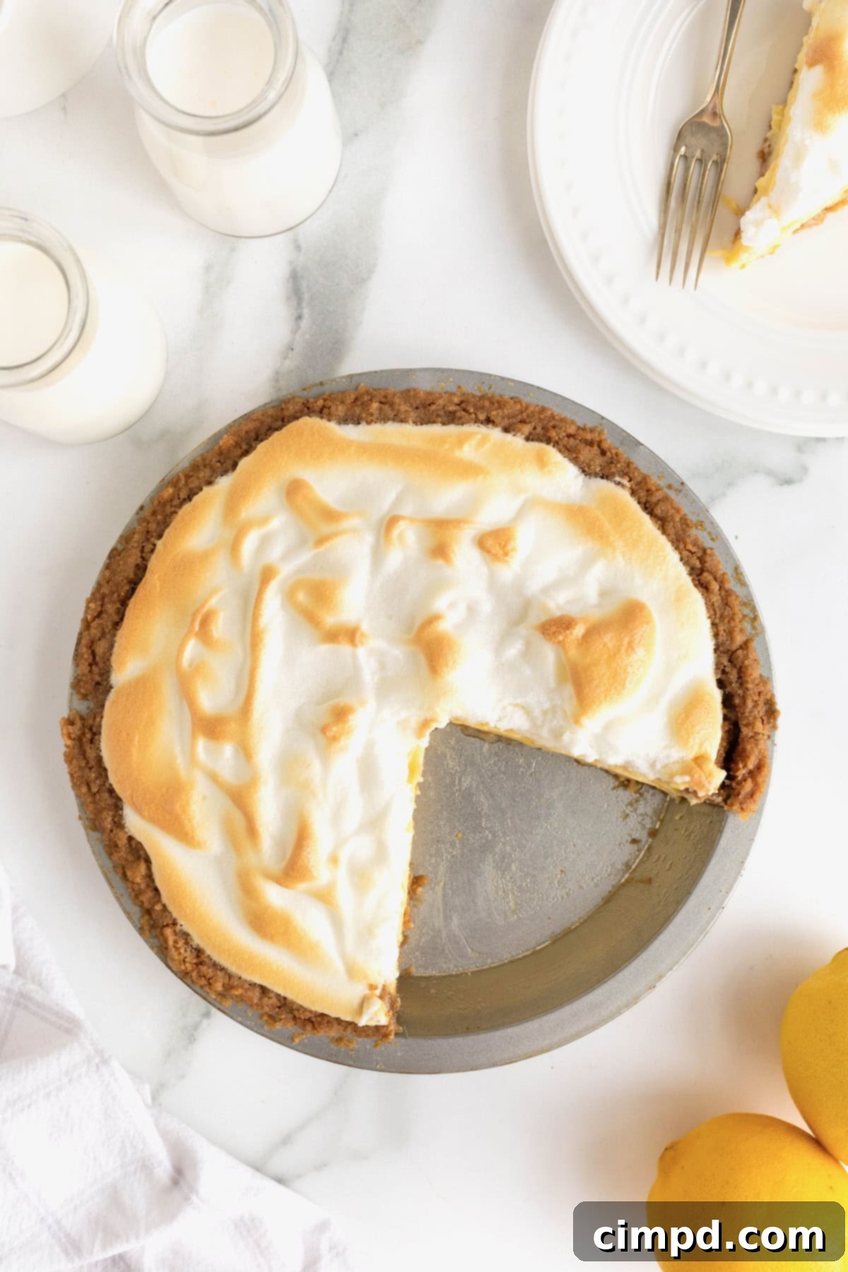 Zesty Meringue Dream 10 A beautifully baked Lemon Meringue Pie in an aluminum pie plate, resting on a white marble counter. Two perfect slices have been carefully removed from the bottom right, inviting enjoyment.