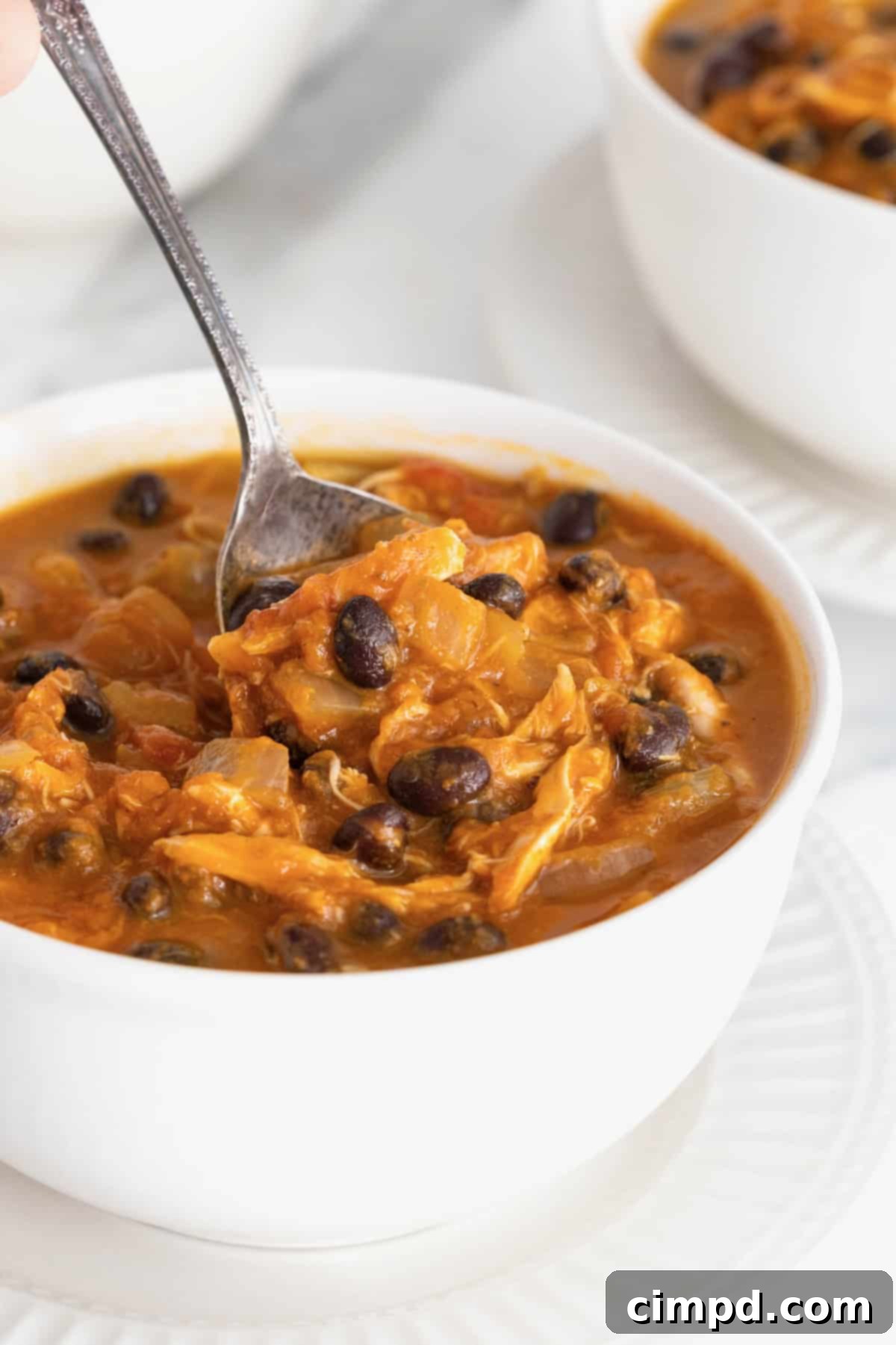 Harvest Pumpkin Chicken Chili 3 A white soup bowl of chicken pumpkin chili with a spoon full being lifted out.