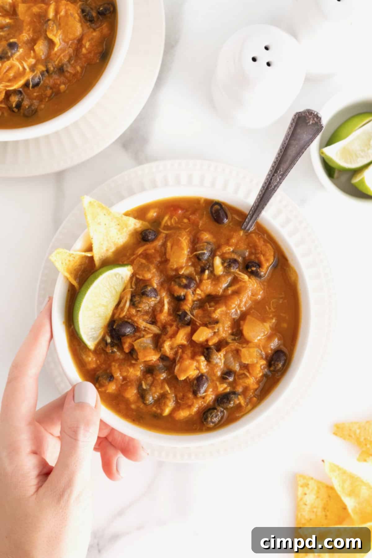 Harvest Pumpkin Chicken Chili 4 A hand touching a white bowl of chicken pumpkin chili.