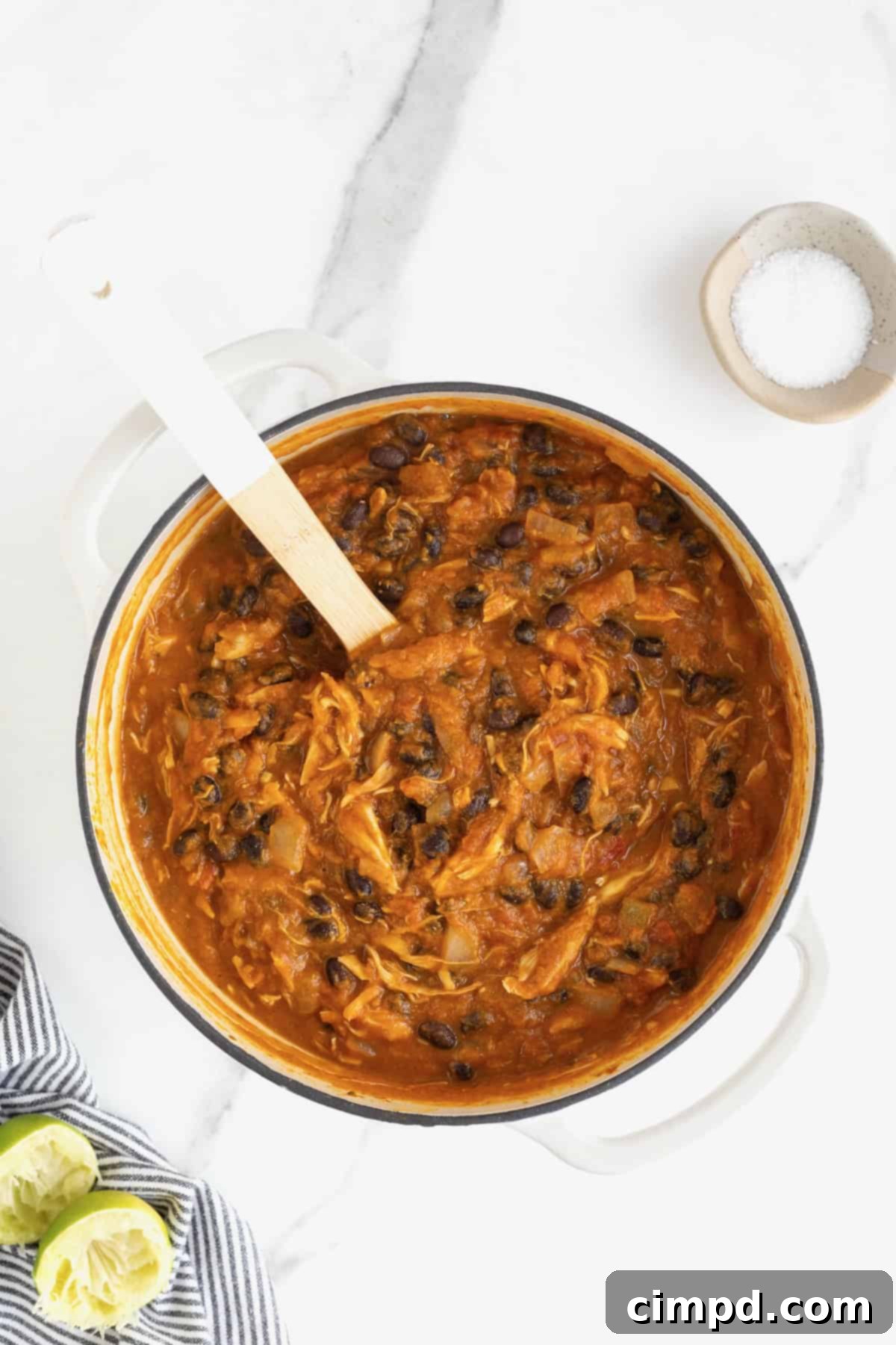 Harvest Pumpkin Chicken Chili 9 A white Dutch oven of chicken pumpkin chili on a white marble counter. There is a wooden spoon with a white handle sticking out of the pot.