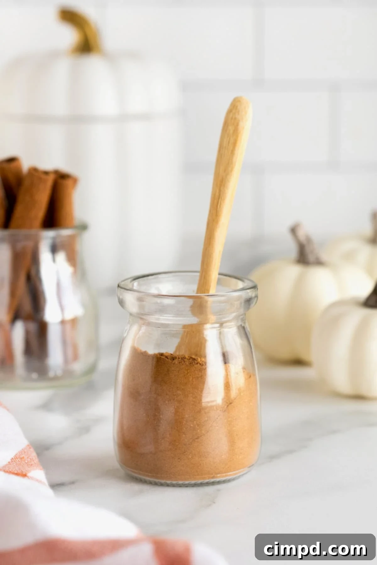 Make Your Own Pumpkin Pie Spice 3 A beautifully labeled glass jar of homemade pumpkin pie spice, ready for use, sits on a rustic wooden cutting board next to a small wooden spoon, highlighting its natural appeal.