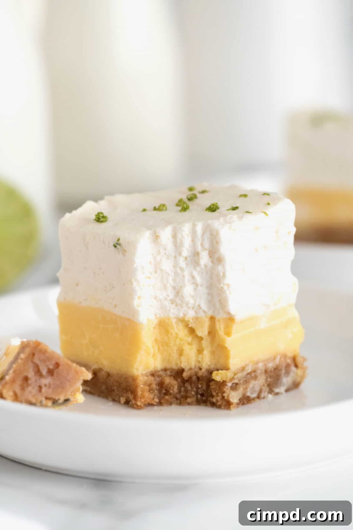 A key lime pie bar on a small white plate. There's a fork with a bite on it next to the bar.