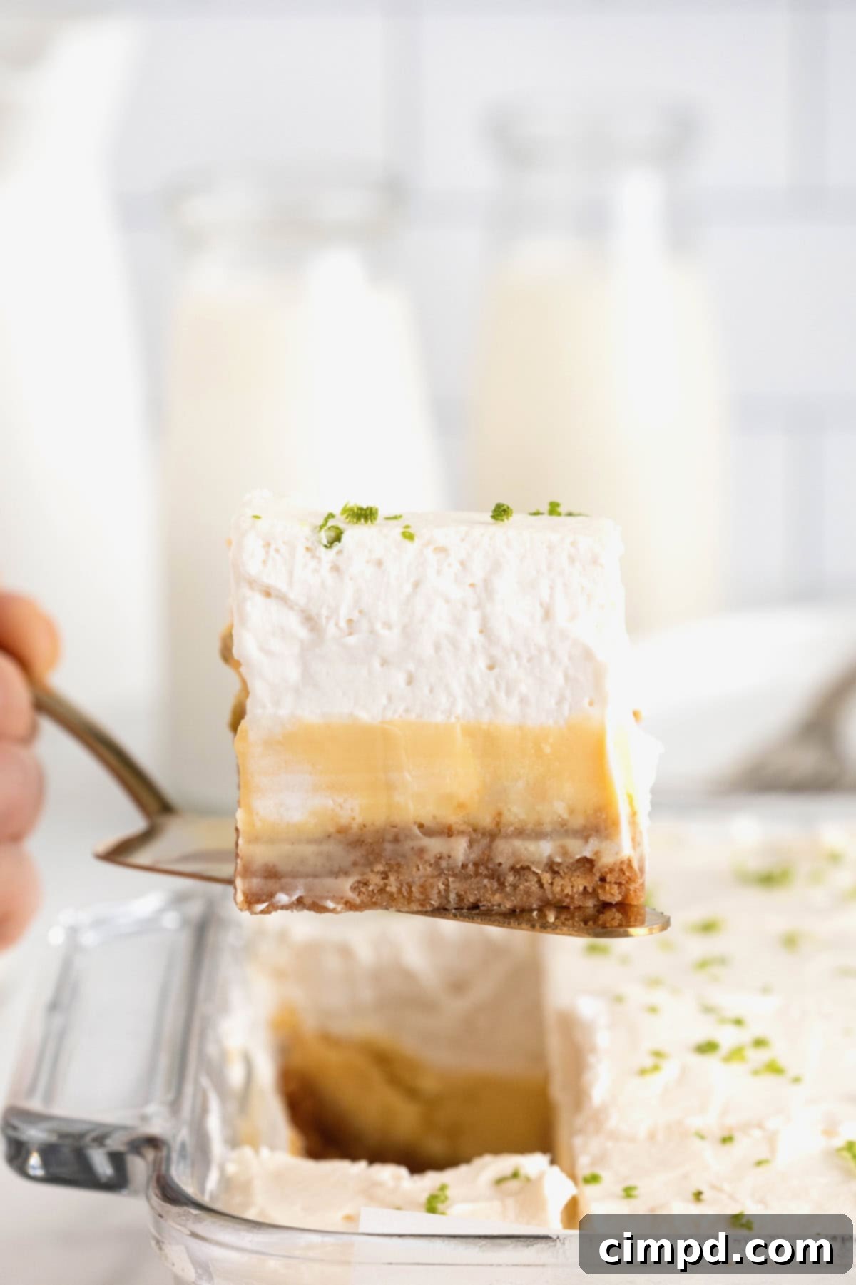 A key lime pie bar being lifted from a square glass baking dish on a metal spatula.