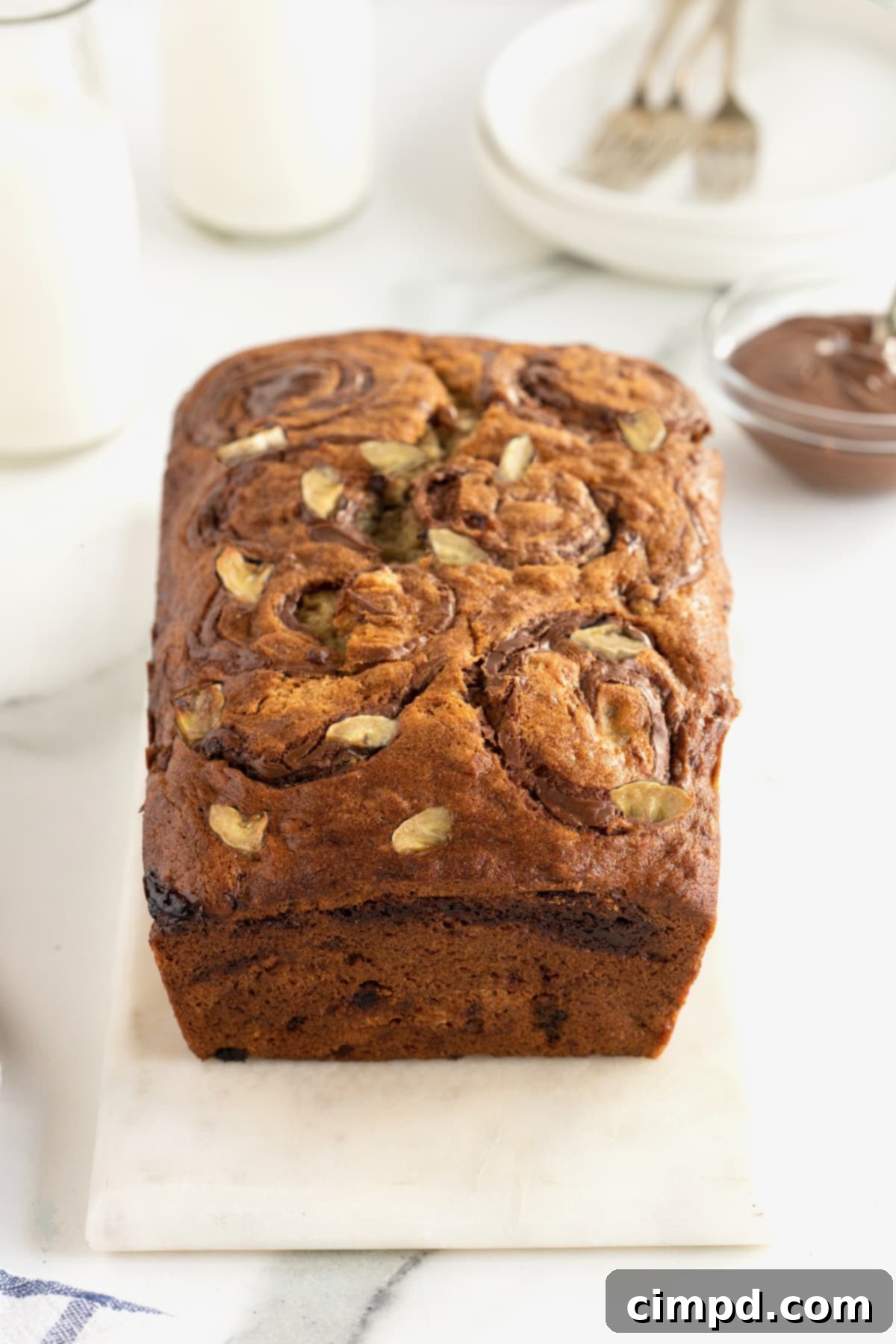 A freshly baked, golden-brown loaf of banana bread sitting on a elegant white and gray marble counter, ready for slicing and storage.