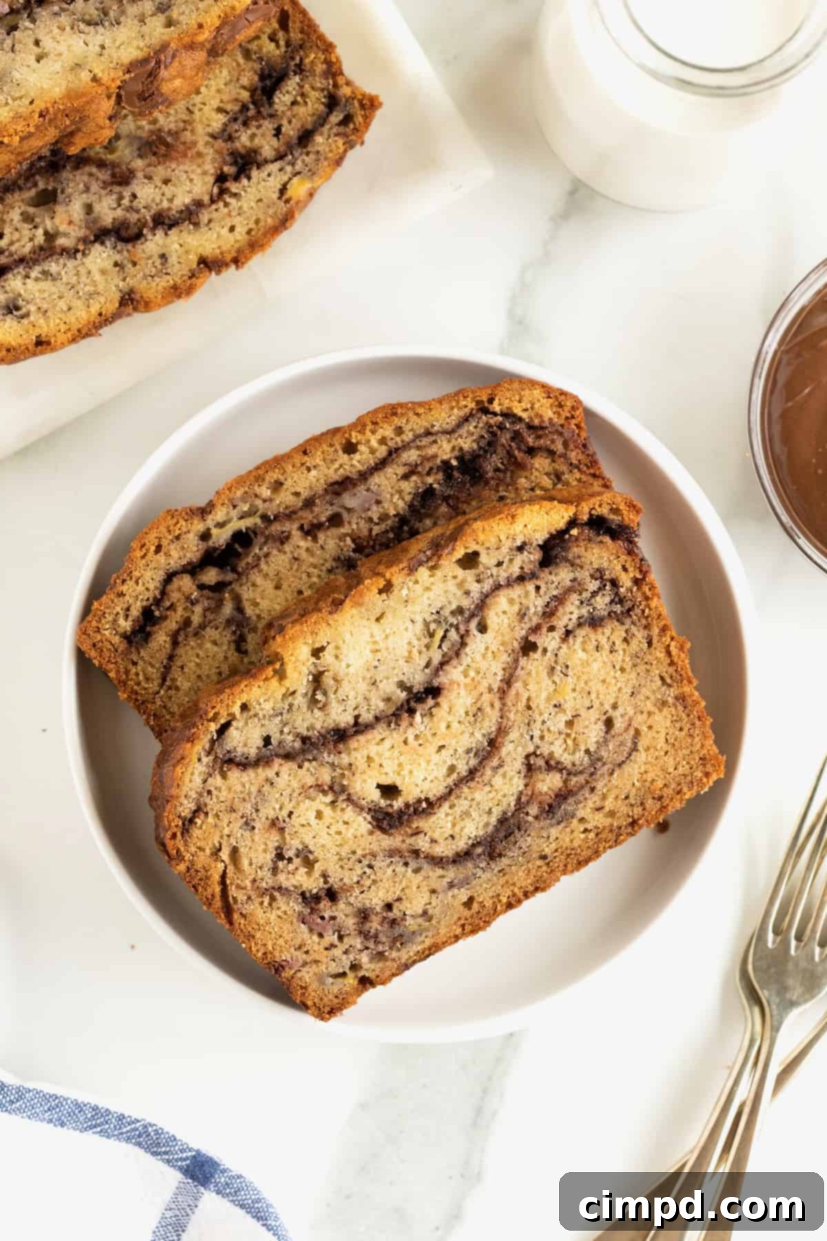 Two generous slices of Nutella swirled banana bread arranged artfully on a pristine white rimmed plate, showcasing the intricate chocolate-hazelnut patterns.