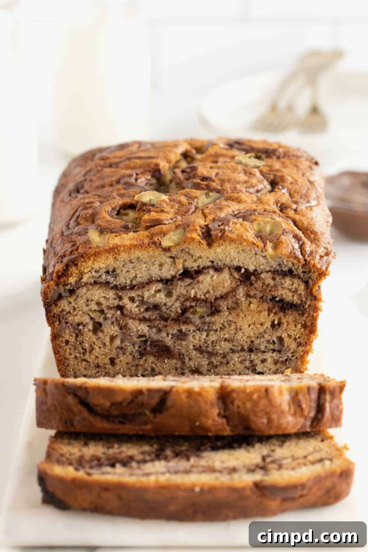 A large, rustic loaf of Nutella swirled banana bread, freshly baked and sliced, sitting on a rectangular white serving platter, highlighting the delectable swirls of Nutella.