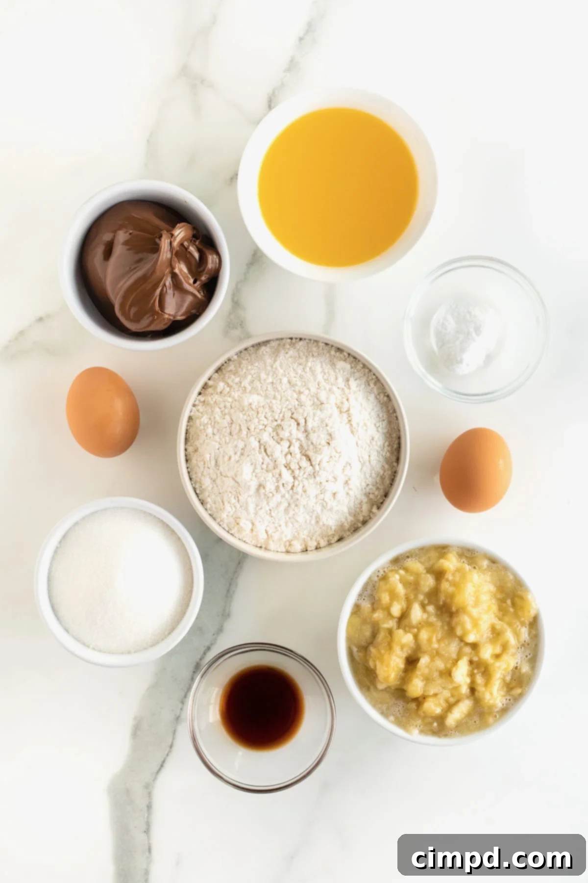 All the essential ingredients for Nutella swirled banana bread neatly arranged in small white dishes on a clean white marble counter, ready for baking.