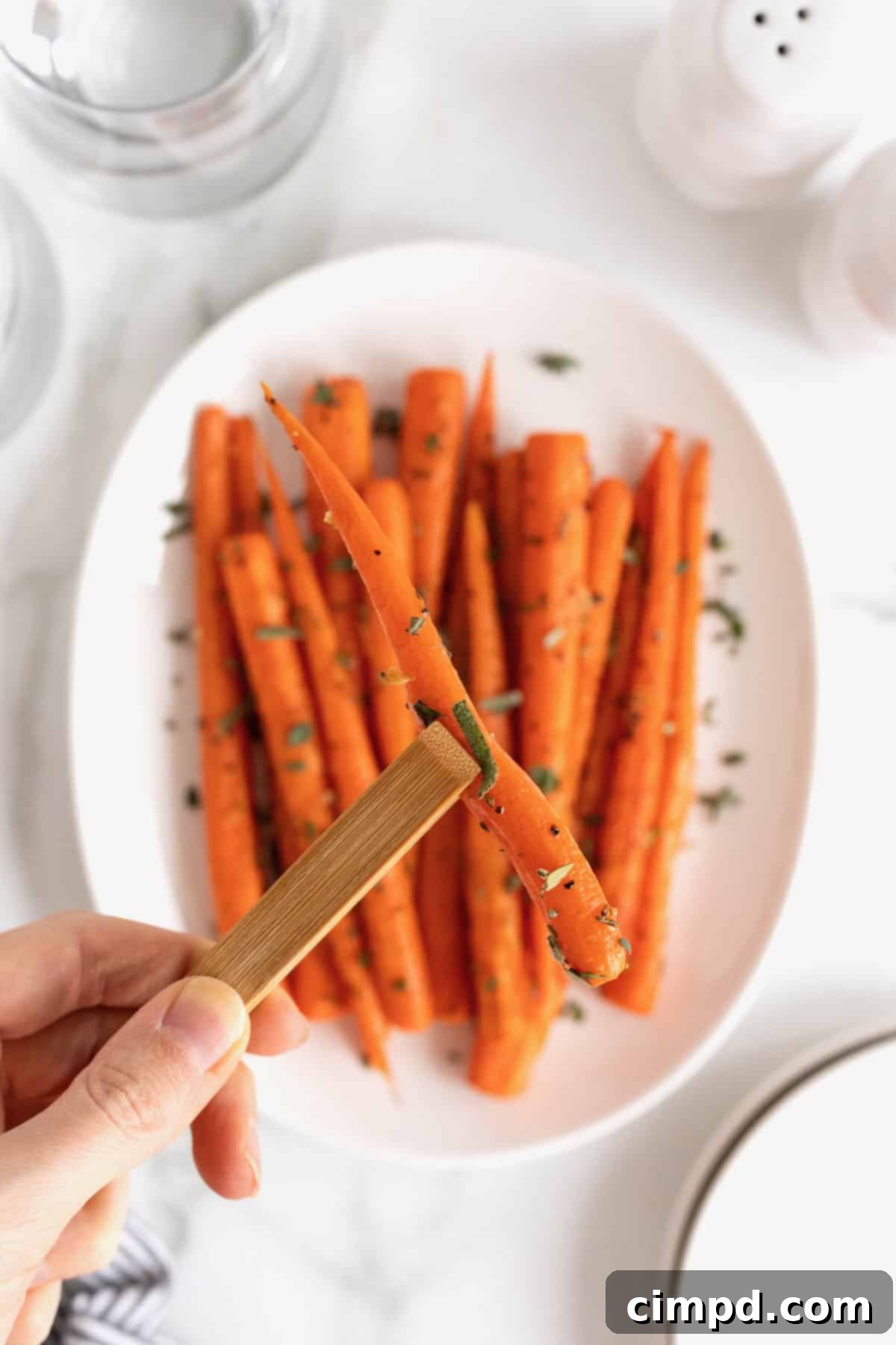 Golden Roasted Carrots 4 A hand gently holds a roasted carrot with a pair of elegant wooden tongs, highlighting its perfectly caramelized texture.