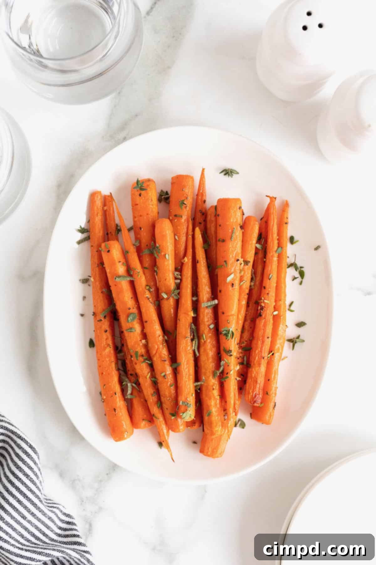 Golden Roasted Carrots 7 An oblong white serving platter brimming with freshly roasted carrots, beautifully garnished with a scattering of vibrant chopped herbs.