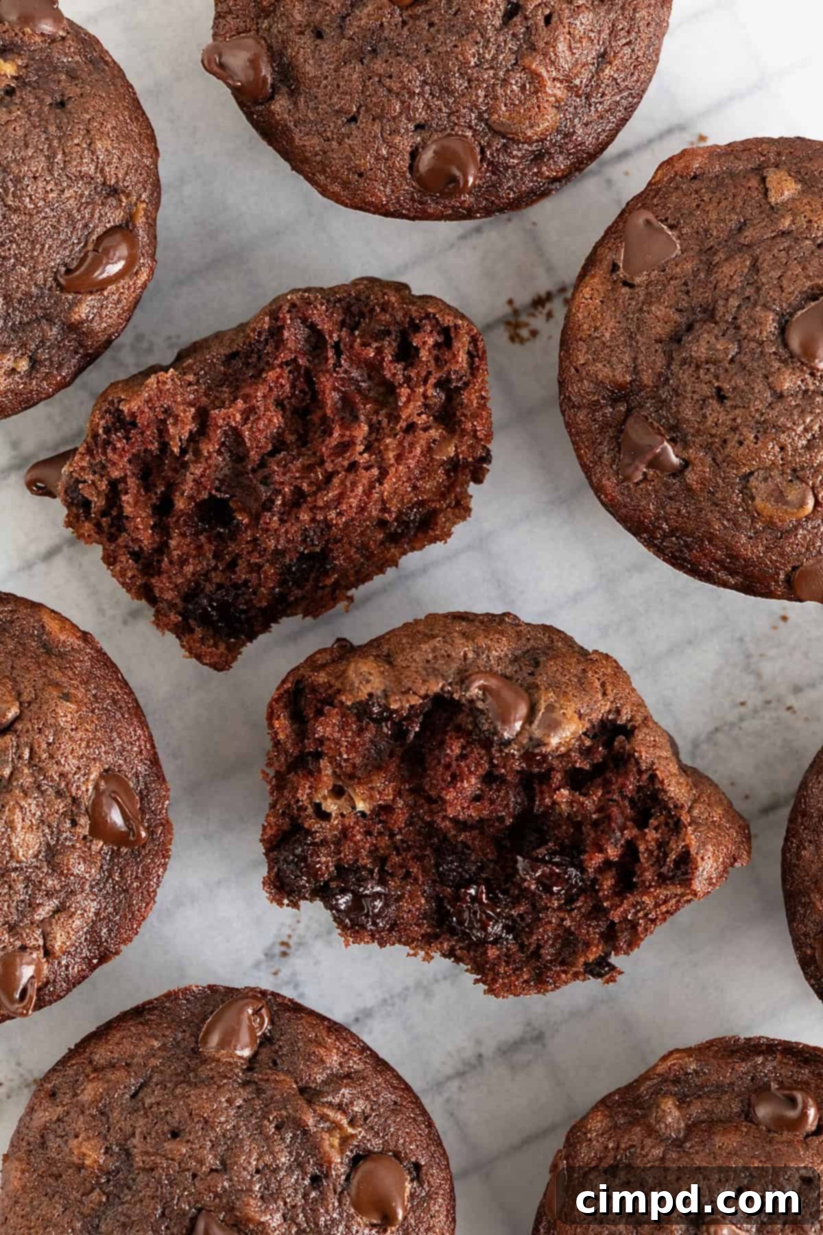 Chocolate Banana Dream Muffins 9 A collection of delectable chocolate banana muffins resting on a parchment-lined cooling rack, with one muffin elegantly torn in half to showcase its tender, moist interior and abundant chocolate chips.