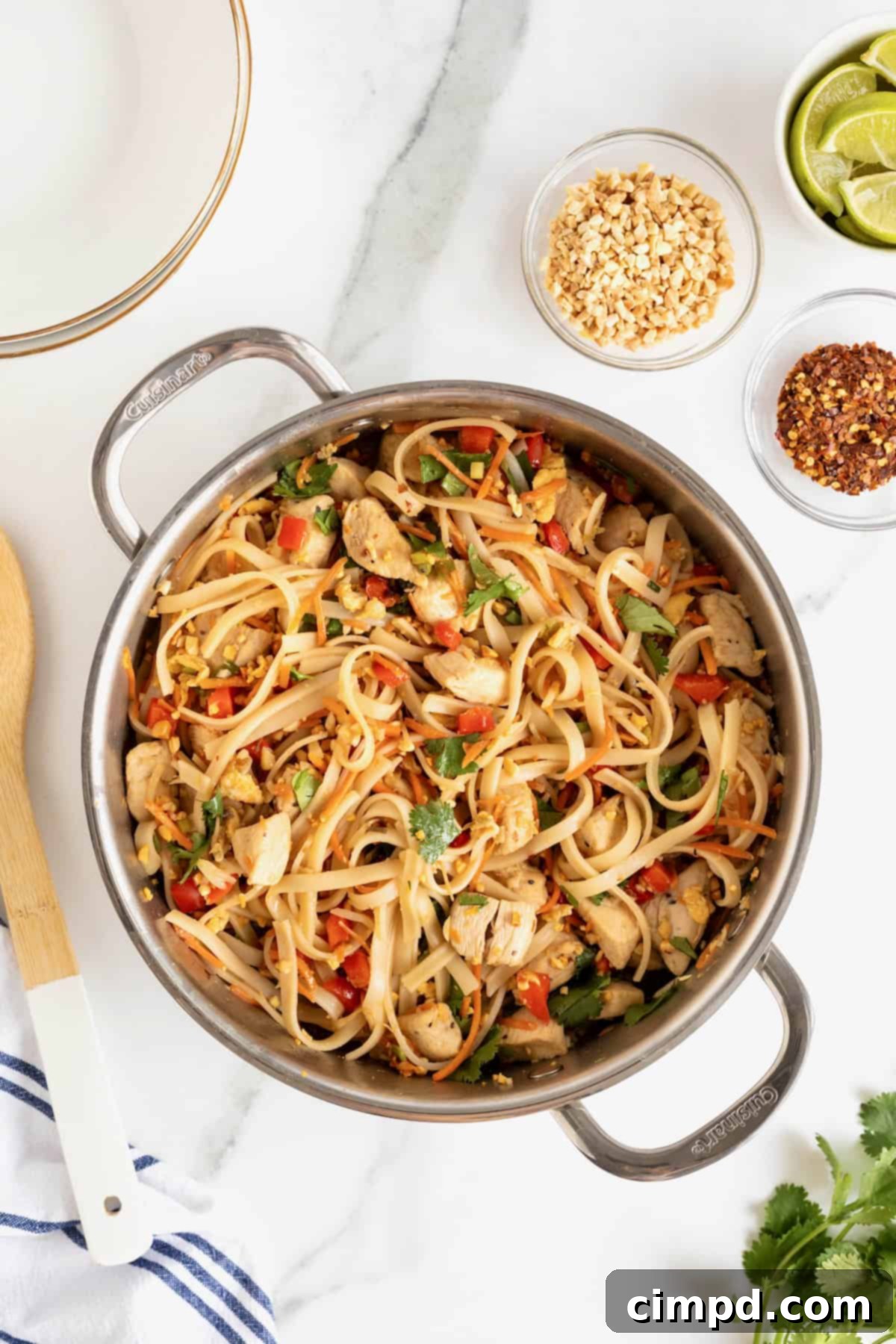 A stainless steel pot of chicken pad Thai on a white marble counter, showcasing the vibrant colors of the noodles, chicken, and vegetables.