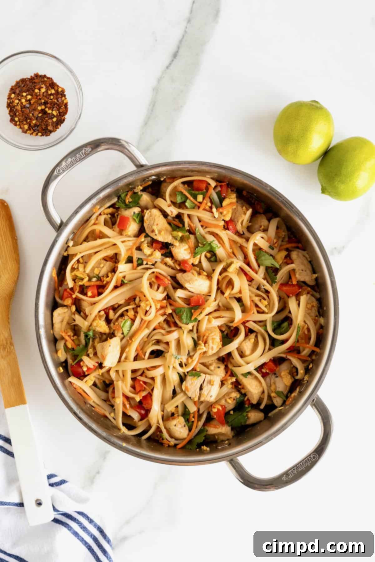 A stainless steel pot filled with perfectly cooked chicken pad Thai, showcasing its rich colors and textures, ready to be served on a pristine white marble counter.