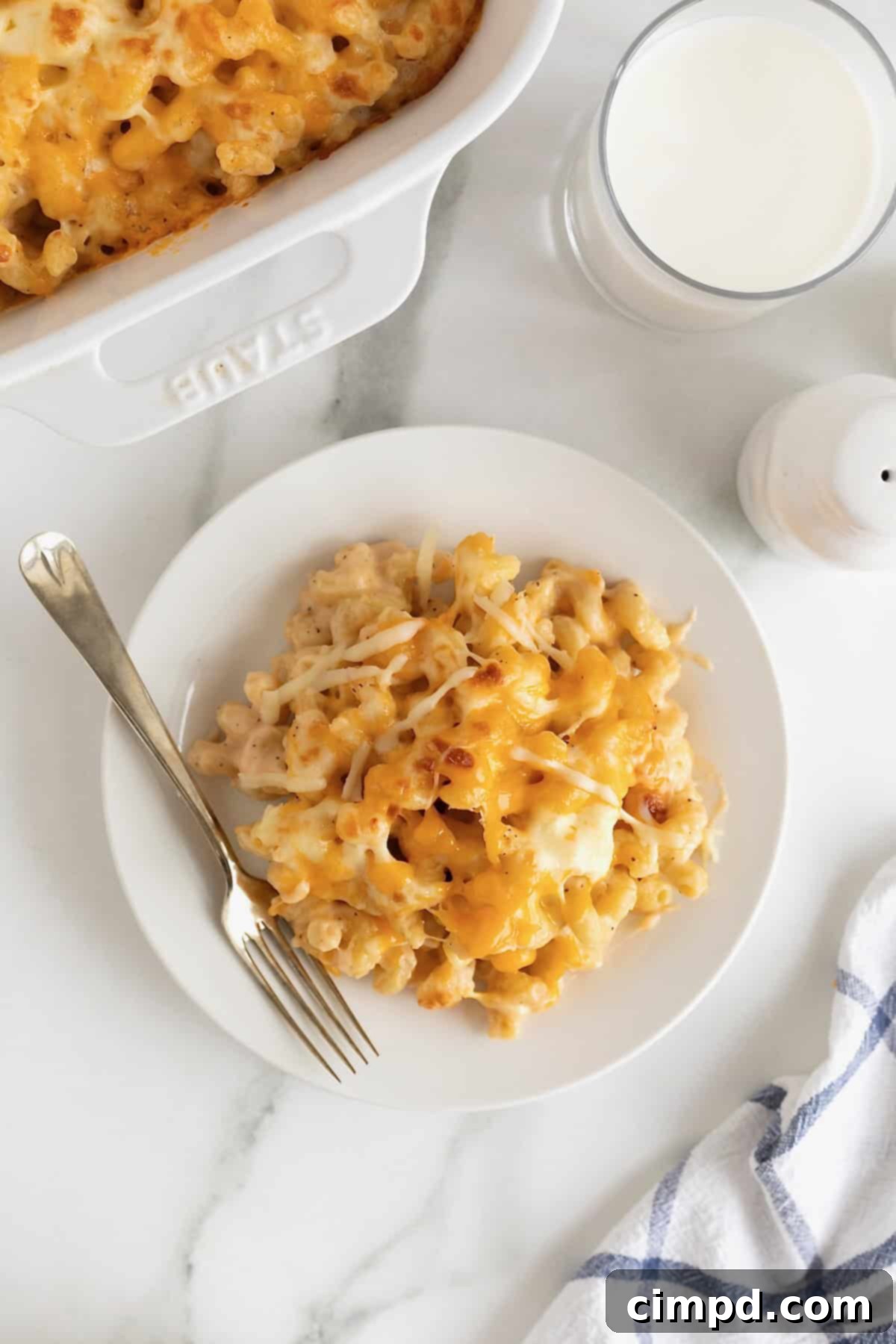 A white dinner plate of baked macaroni and cheese with a metal fork resting on the side, ready to be enjoyed.