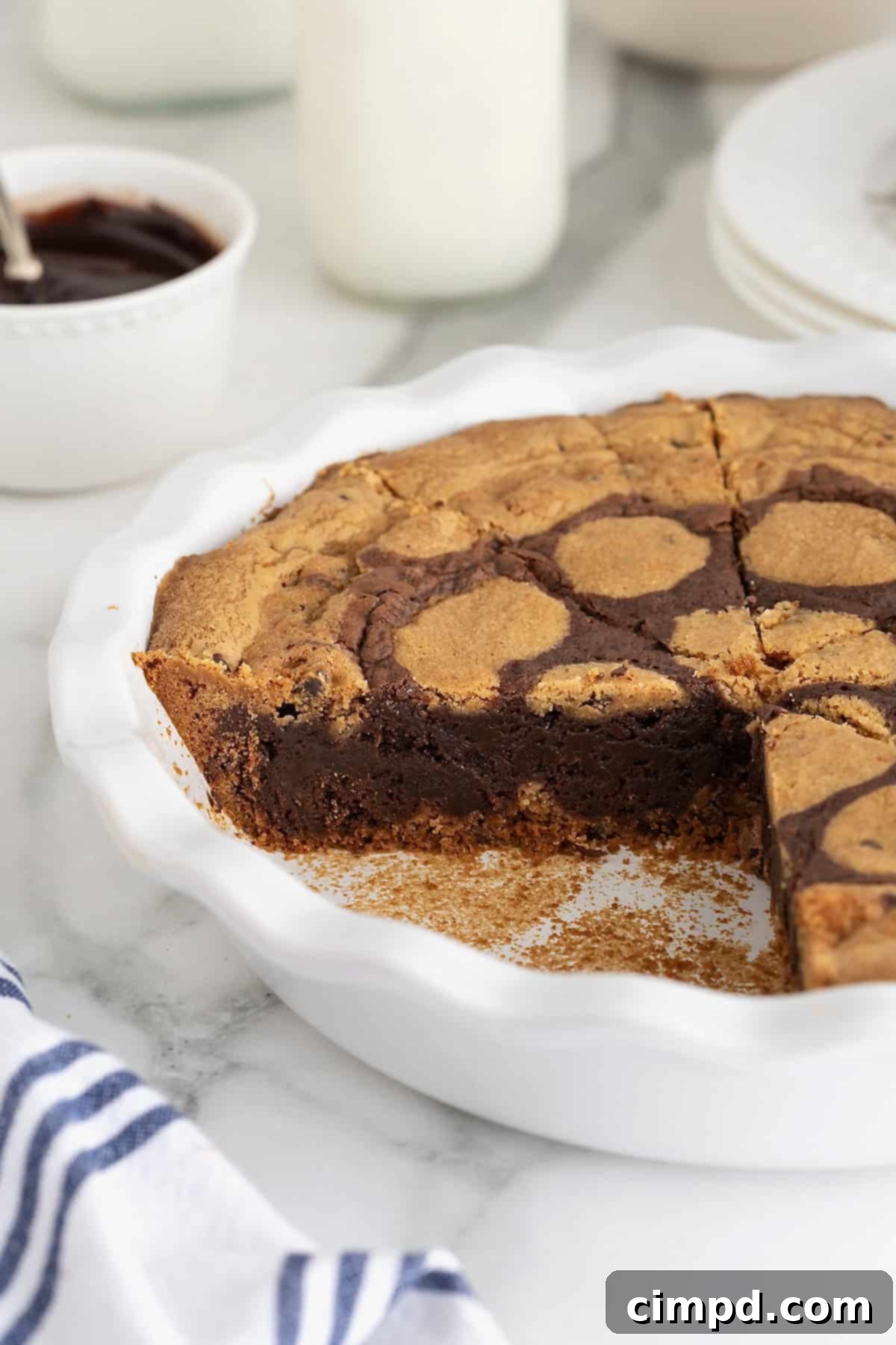 A freshly baked brookie pie cooling in a white scalloped porcelain pie plate, with one perfect slice already removed.