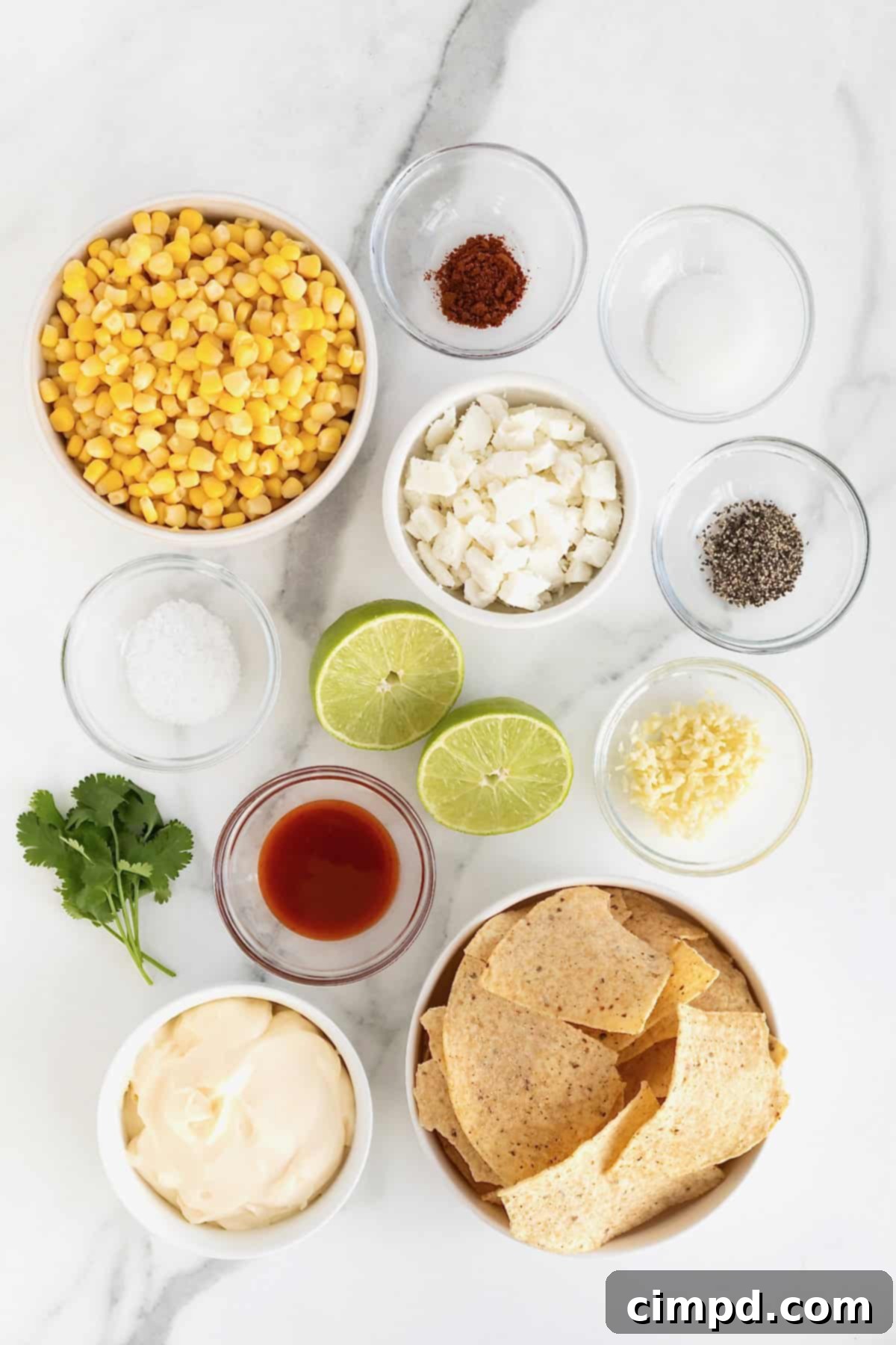 A collection of fresh ingredients laid out on a wooden surface, including corn kernels, lime, mayonnaise, hot sauce, and cotija cheese, ready to make roasted corn elotes dip.