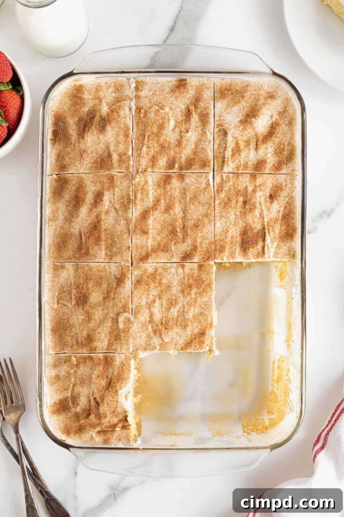 A glass baking dish of tres leches cake with several pieces missing.