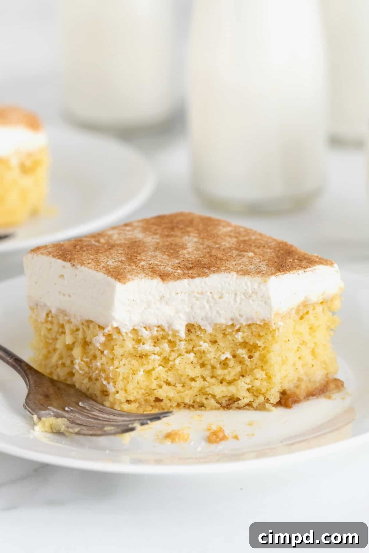A square of tres leches cake on a white dessert plate with a fork next to it.