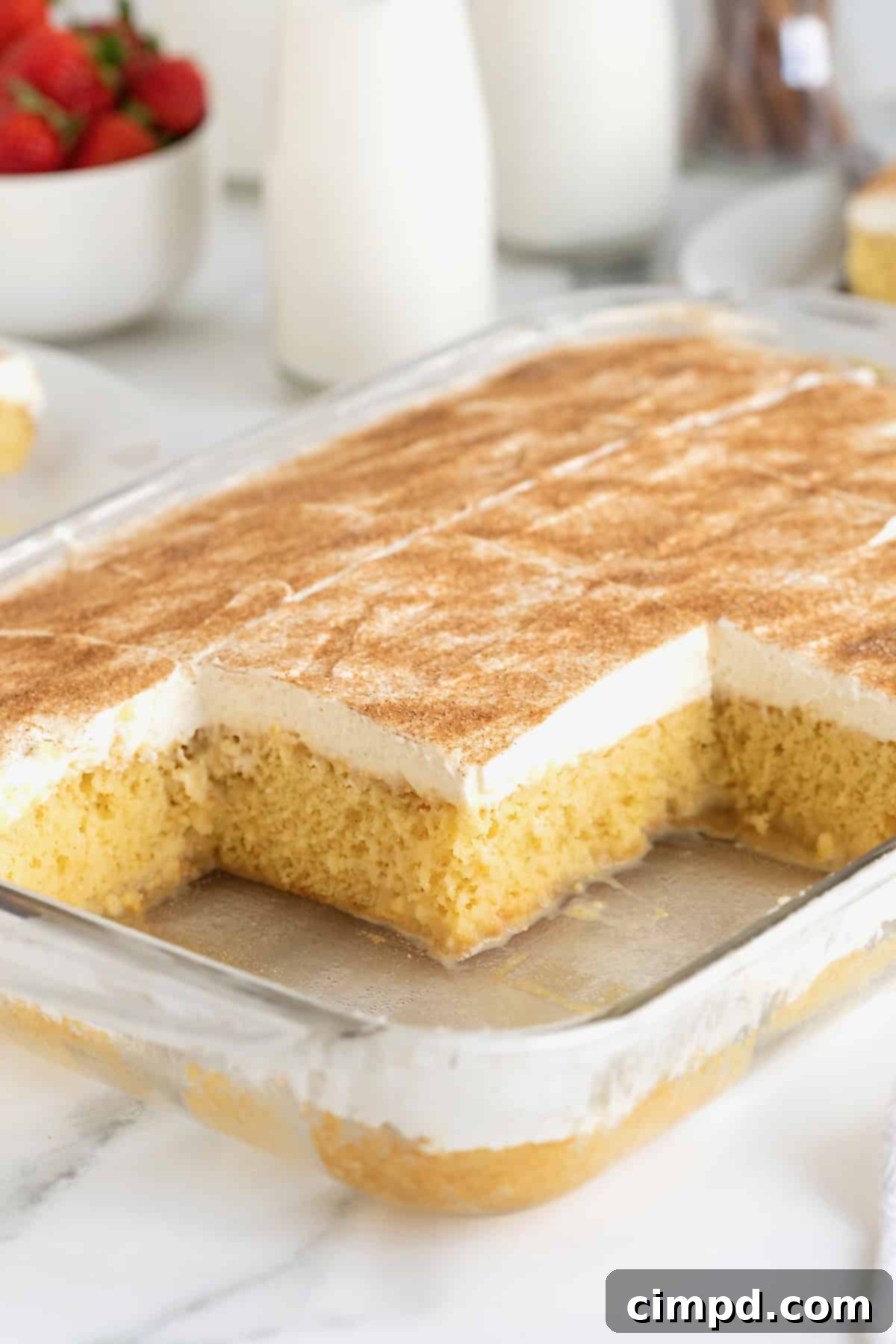 A glass baking dish of tres leches cake with several pieces missing.