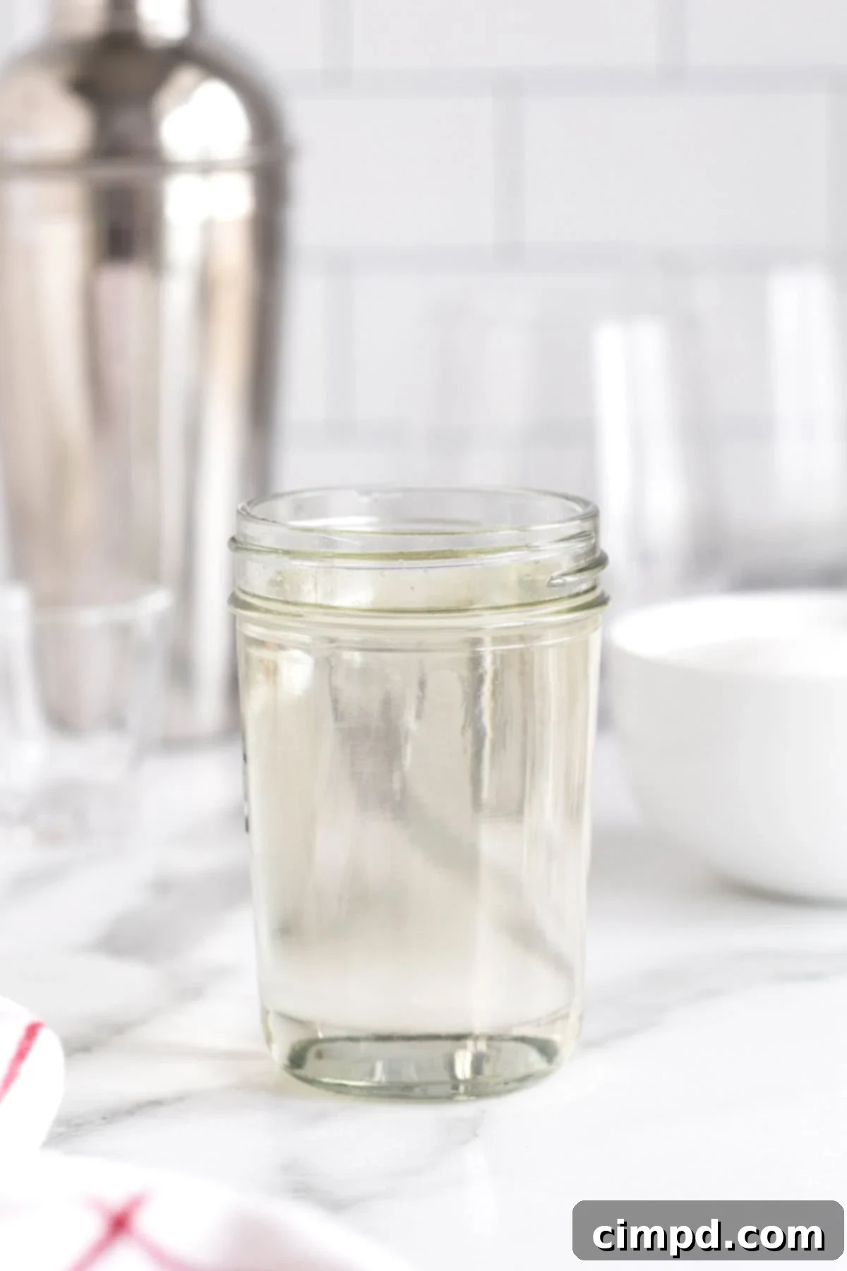 A full mason jar containing homemade simple syrup, sitting on a white marble counter. A perfect depiction of ready-to-use liquid sweetener.