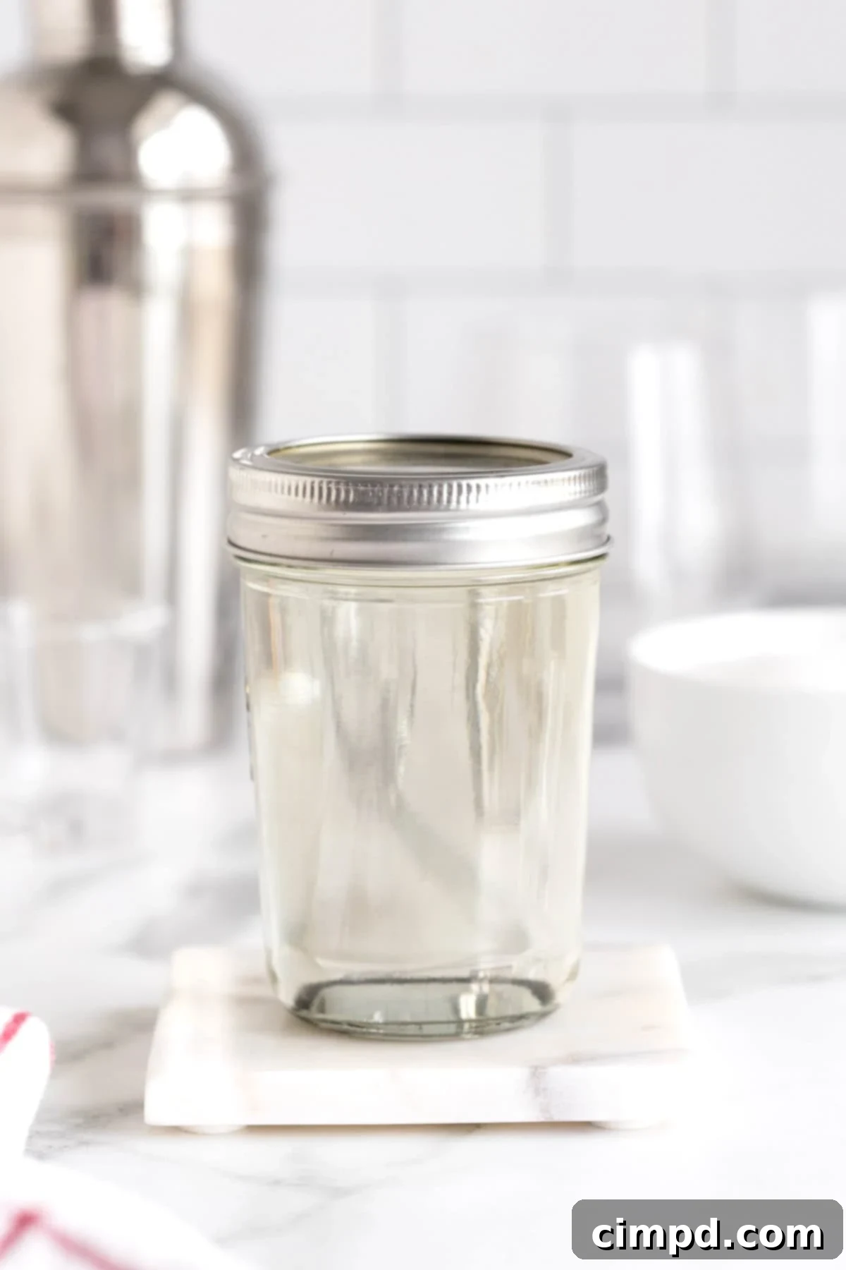 A sealed mason jar containing freshly made simple syrup, placed on a white marble counter, ready for refrigeration and long-term storage.