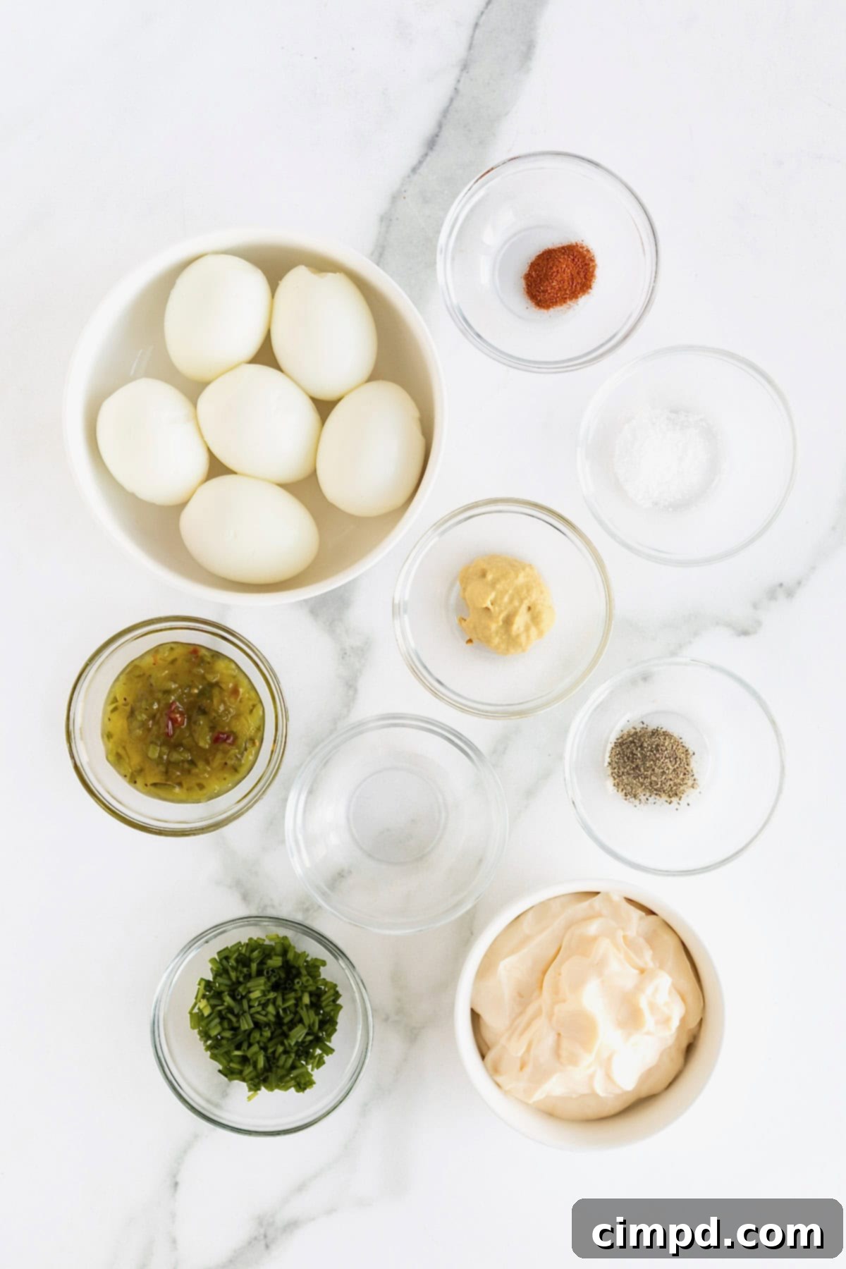 Ingredients to make deviled egg dip in small glass dishes on a white marble counter.